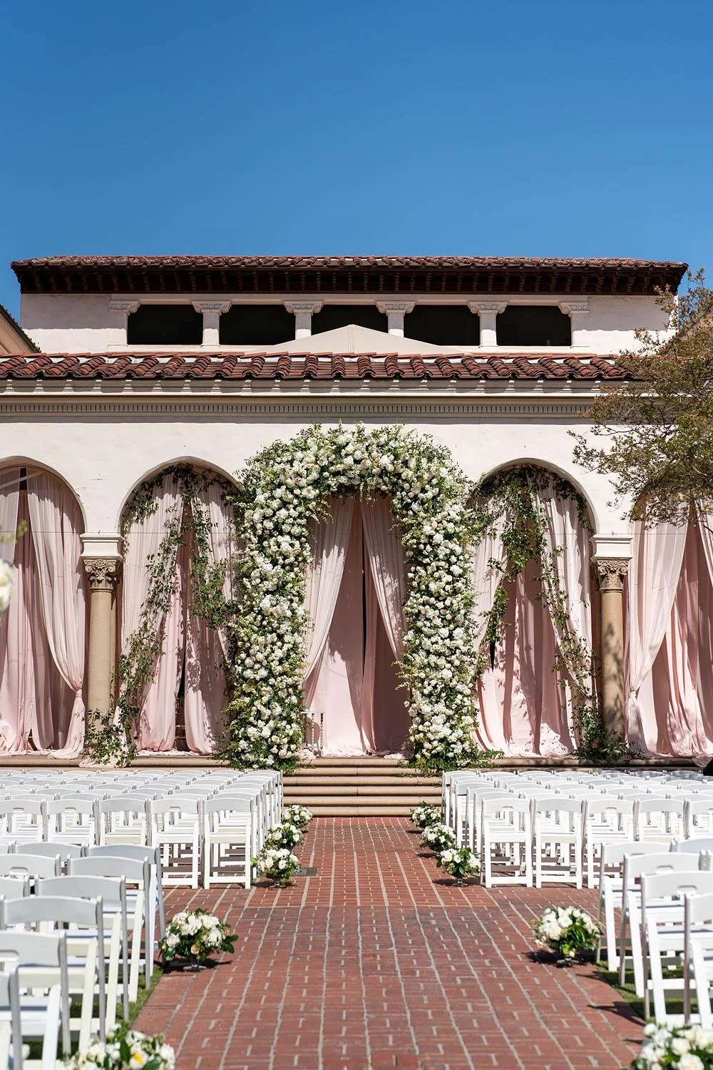 Wedding ceremony floral arch between by pink draped arches in the courtyard at the Athenaeum at Caltech