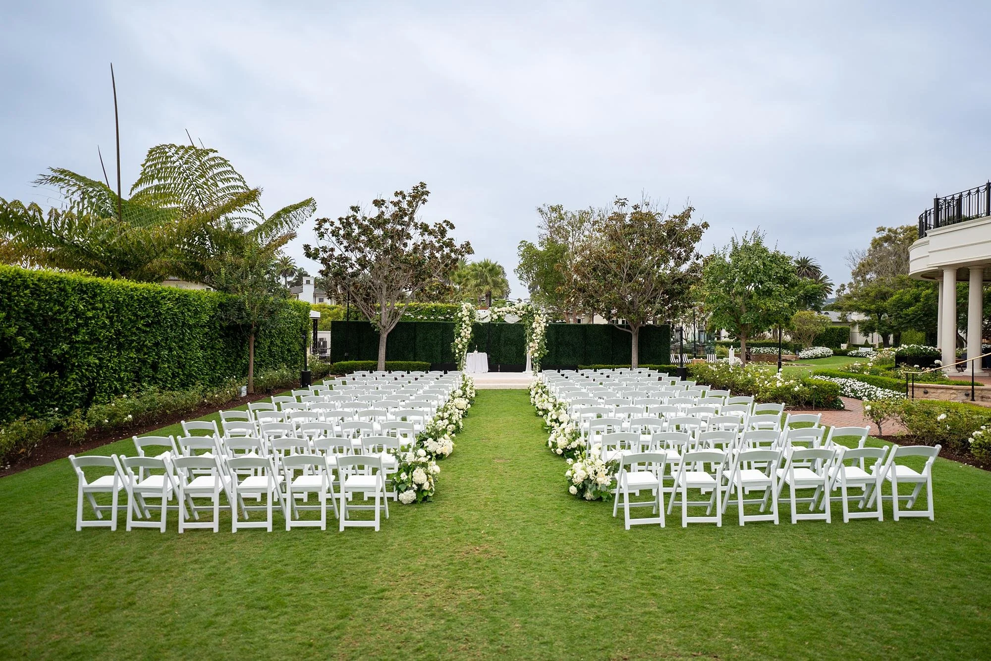 Wide view of a wedding ceremony on the Event Lawn with white florals at Rosewood Miramar Beach