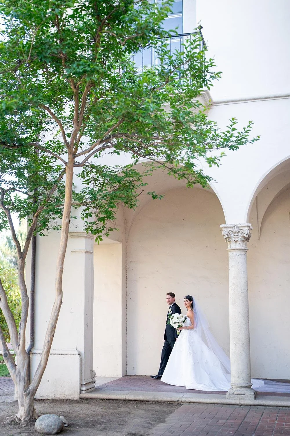 Wedding portraits of bride and groom walking between columns at the Athenaeum at Caltech