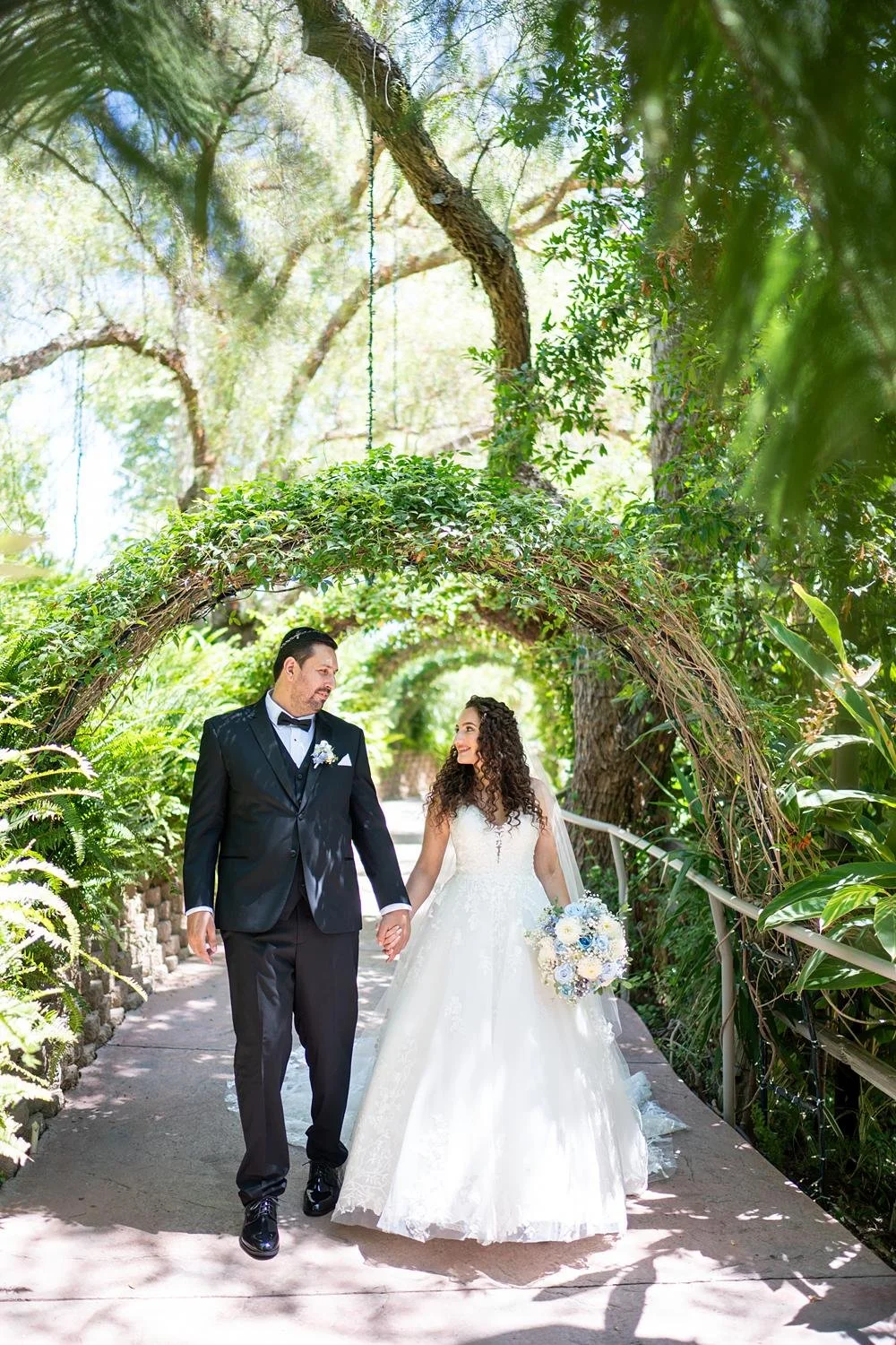 Wedding portraits of bride and groom walking together on a tree-lined path at The Vineyards Simi Valley