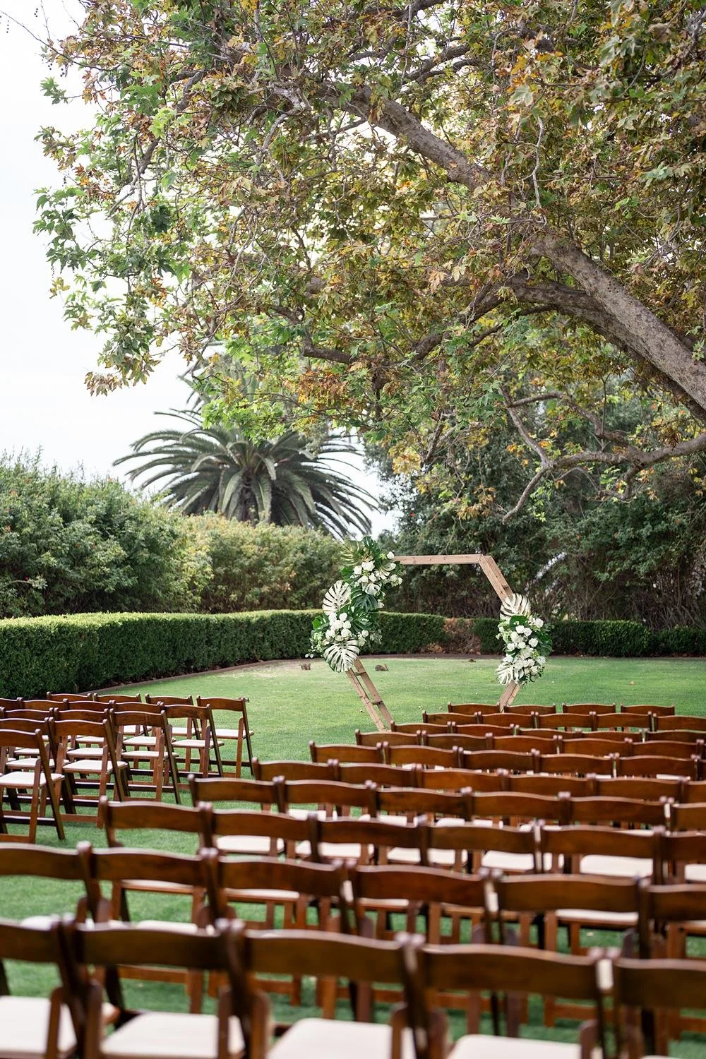 Wedding ceremony at Adamson House featuring a modern arch with tropical leaves