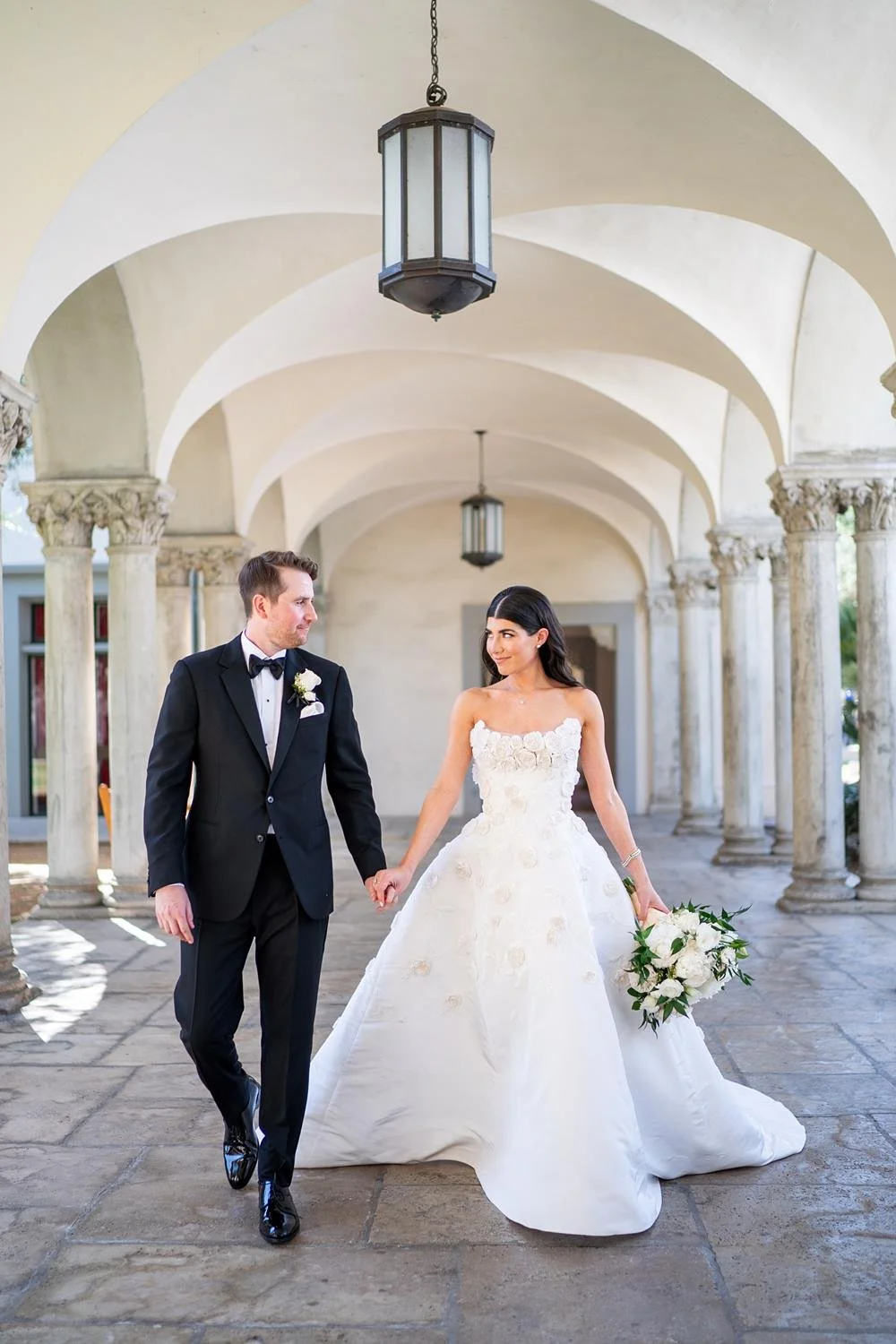 Wedding portraits of couple walking beneath arches and framed by an columns at the Athenaeum at Caltech