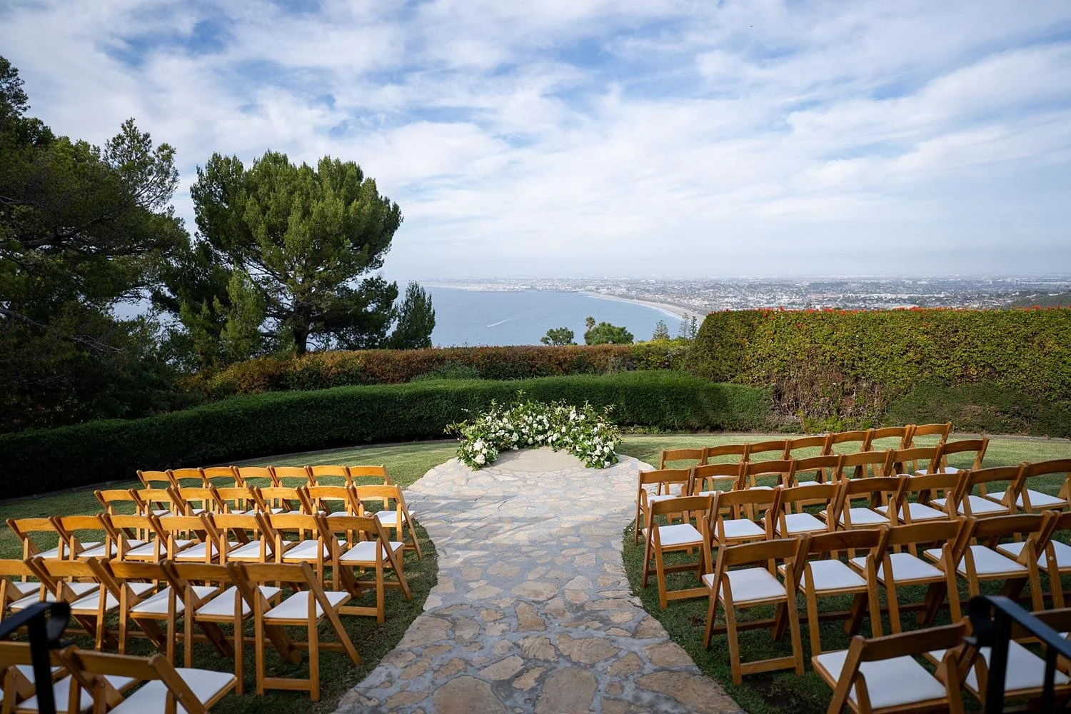 Wedding ceremony on the lawn with white florals and greenery overlooking the coastline at La Venta Inn