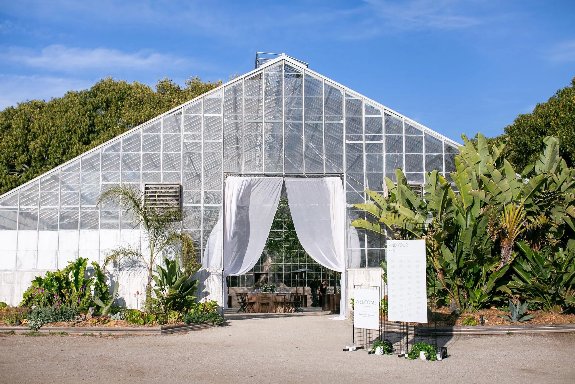Wedding reception greenhouse exterior with entrance draped in white fabric at Dos Pueblos Orchid Farm