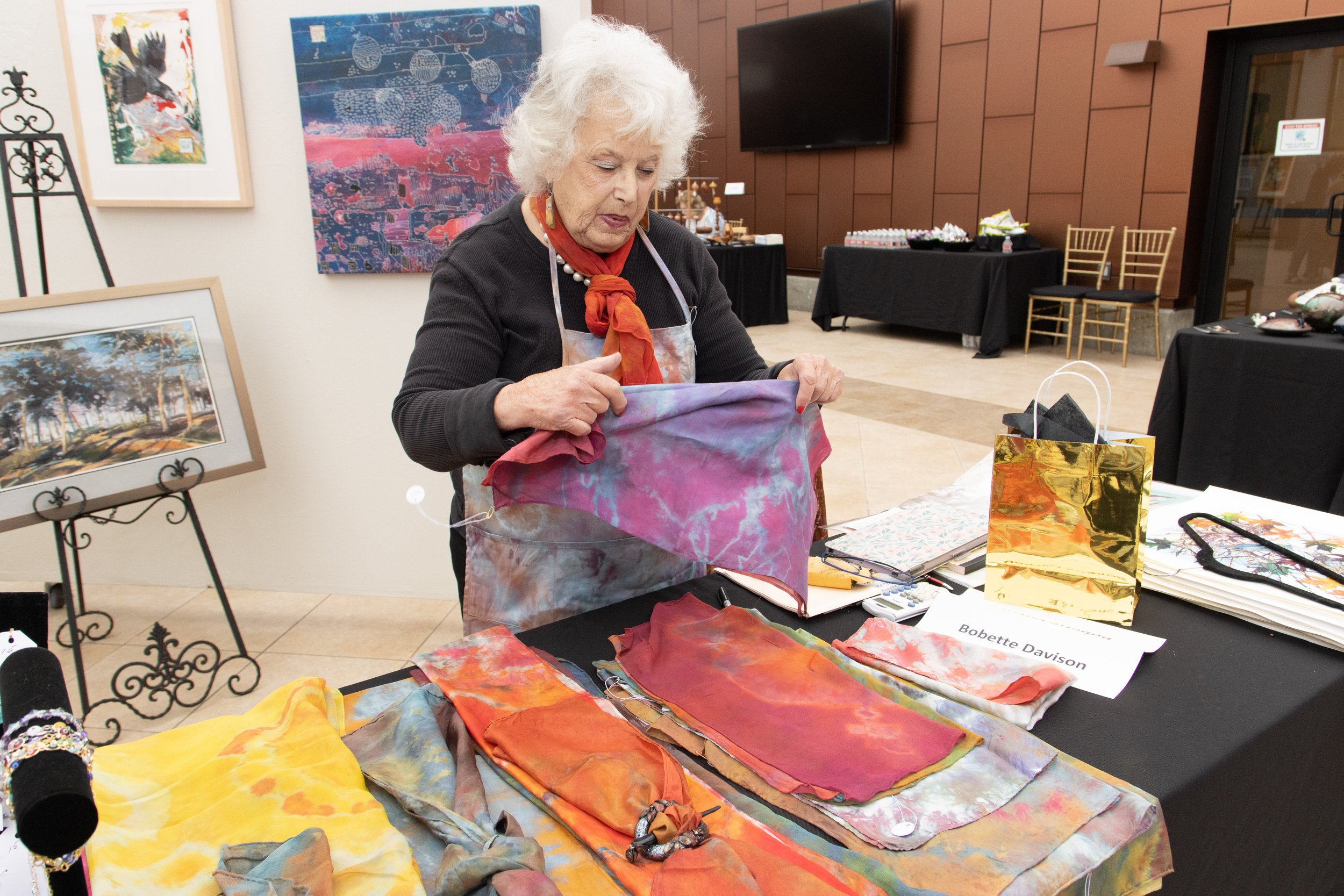 Bobette Davidson displaying her various handmade scarves and framed watercolor art pieces