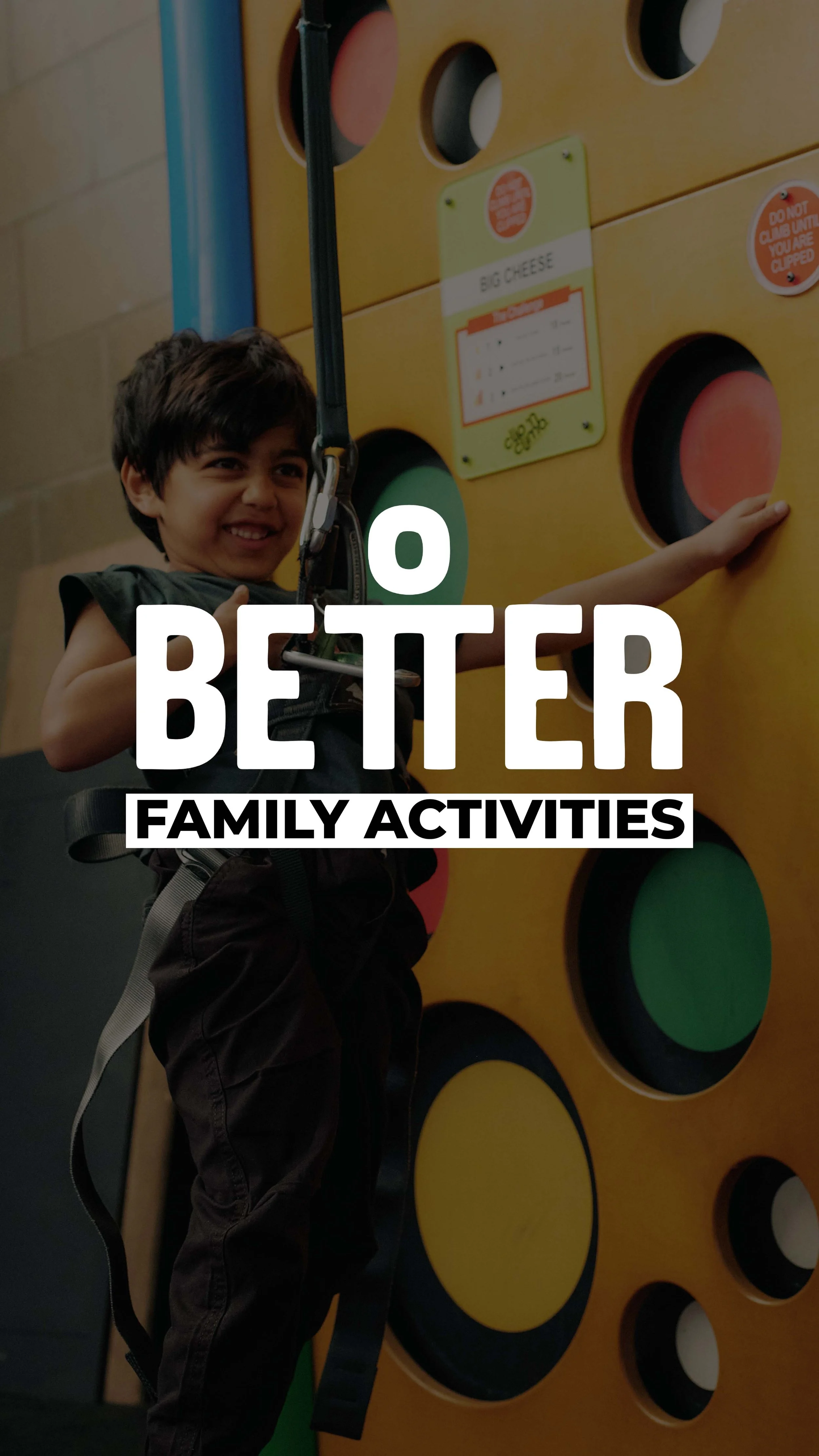 A young boy smiling while reaching towards a colorful wall with circular cutouts at an indoor activity center.