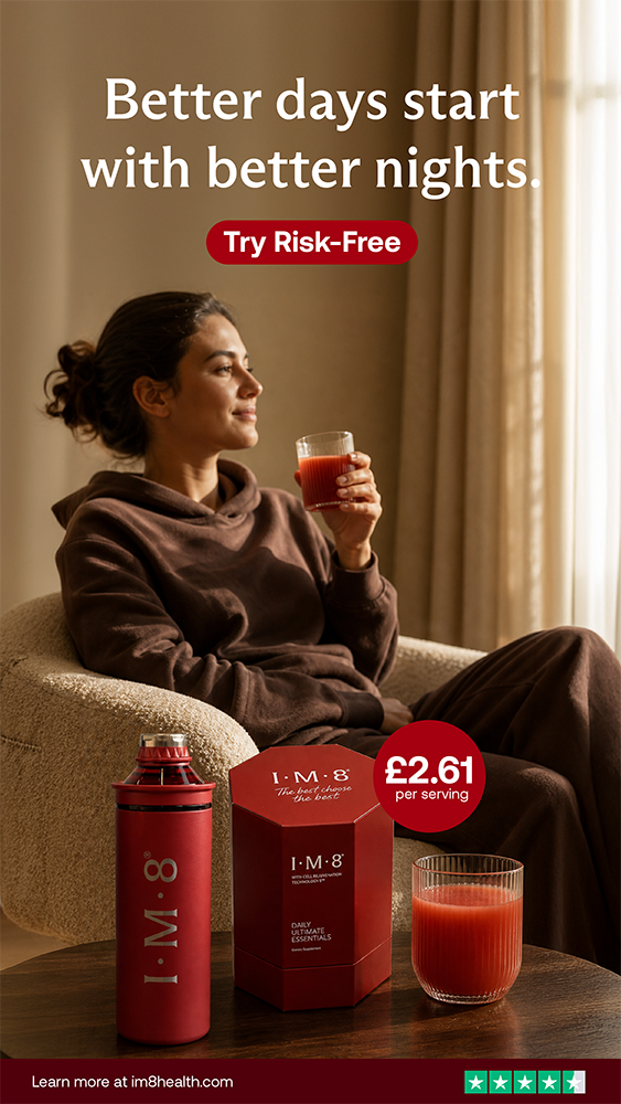 A woman sitting on a beige chair with a blanket, holding a glass of red juice, with a box and bottle of I.M.8 daily essentials on a table in front of her, promoting better days and nights.