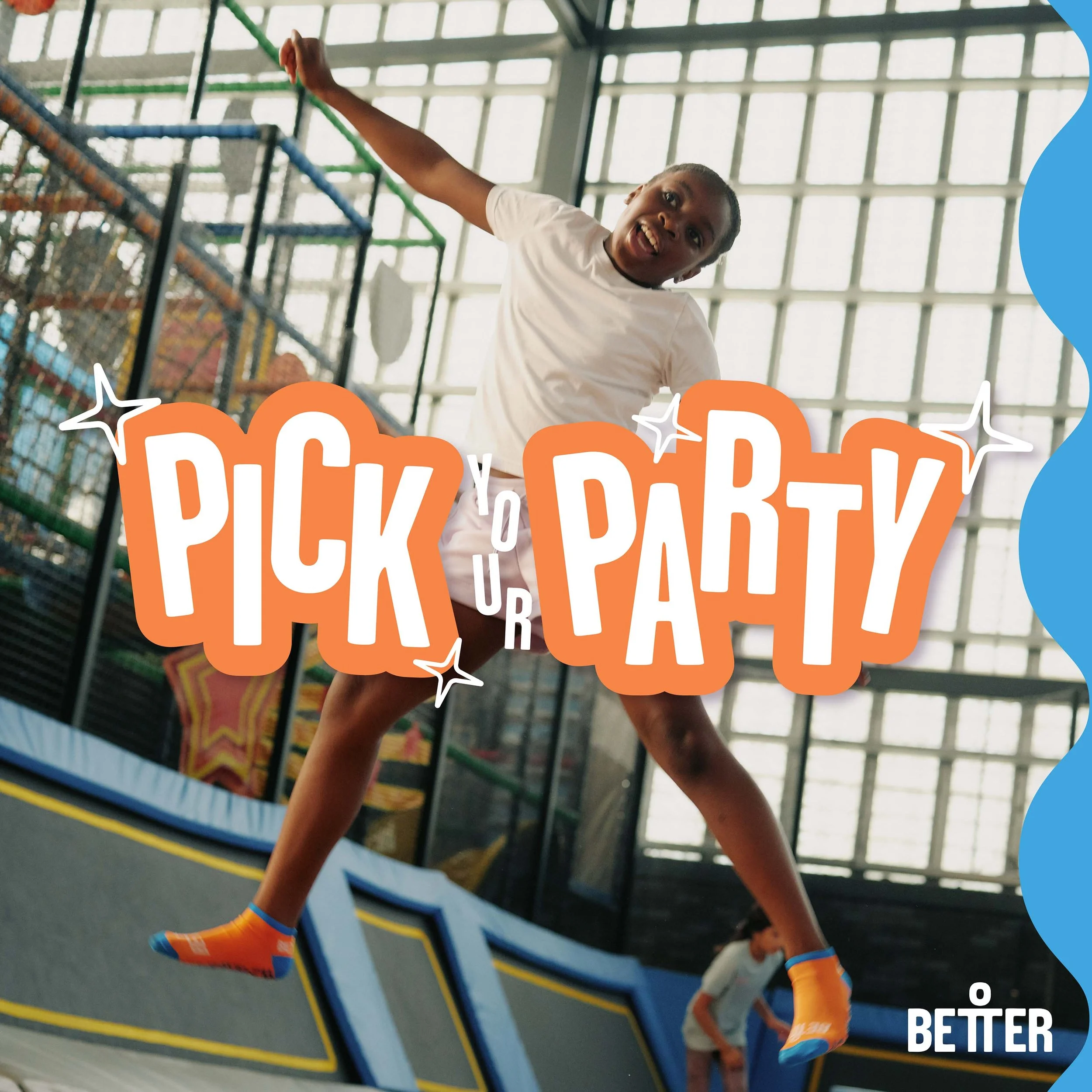 A young boy is jumping on an indoor trampoline, mid-air, with a focused expression. He is wearing bright orange and blue socks and a white shirt. The background shows a high ceiling with large windows and the trampoline structure.