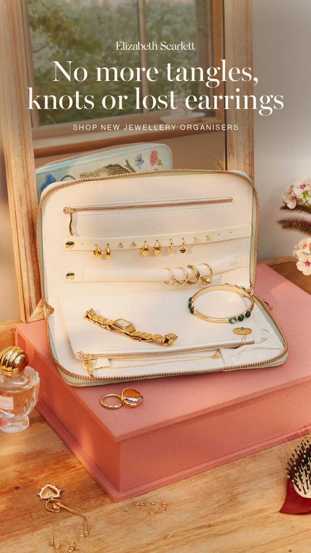An open jewellery case displaying various jewellery items such as earrings, bracelets, and necklaces, with a reflection of a window and trees in the background.