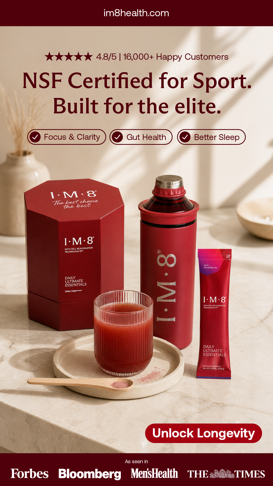 Red container labeled 'I.M.8 Daily Ultimate Essentials' with a matching bottle, packet, and glass of red beverage on a beige countertop, with text promoting health benefits and a quote 'Unlock Longevity' at the bottom.