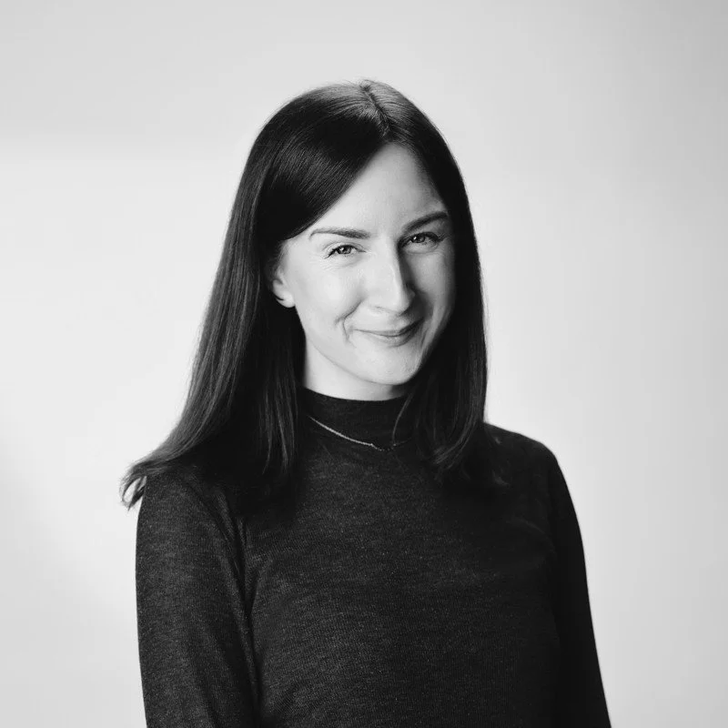Woman with shoulder-length brunette hair, wearing a black turtleneck, smiling directly at the camera.