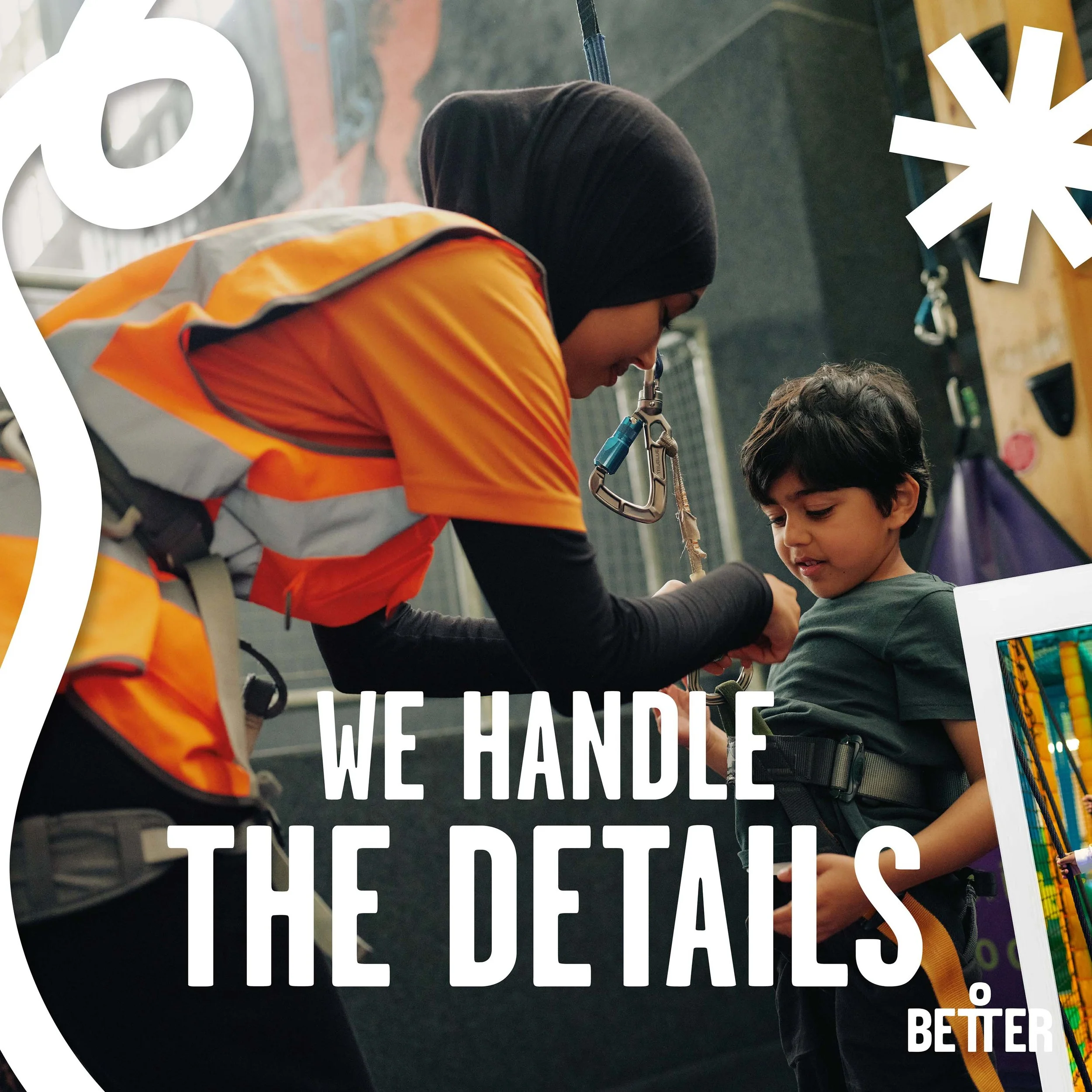 A woman wearing a black hijab and an orange safety vest helping a young boy with dark hair, wearing a black harness, in an indoor climbing gym. The background features climbing walls and gym equipment.