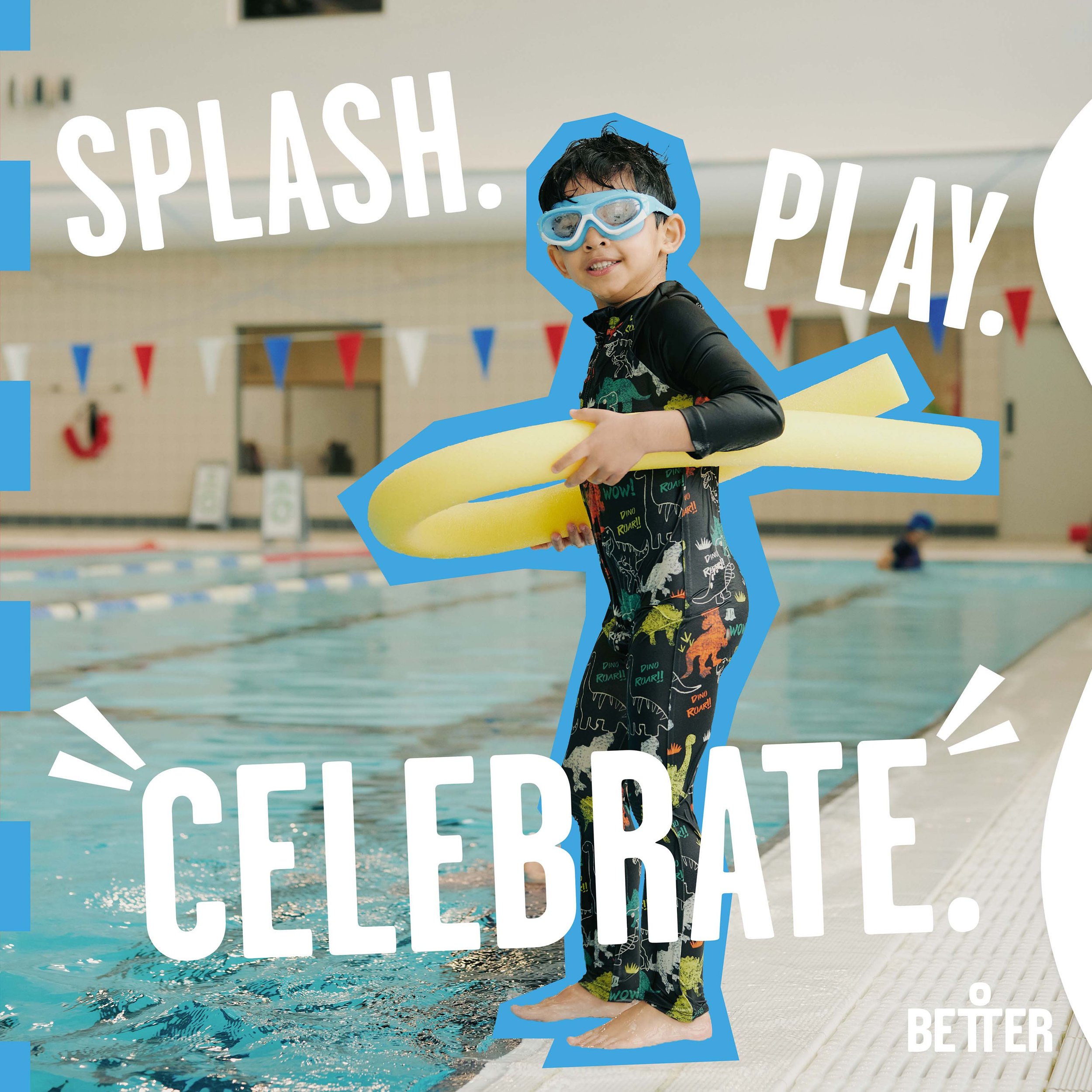 A young boy wearing swimming goggles is standing at the edge of an indoor swimming pool, holding a yellow pool float, with colorful flags hanging in the background.