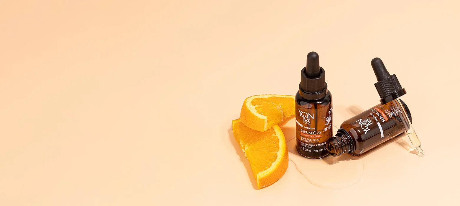 Orange slices and skincare serum bottles with dropper on a light peach background.