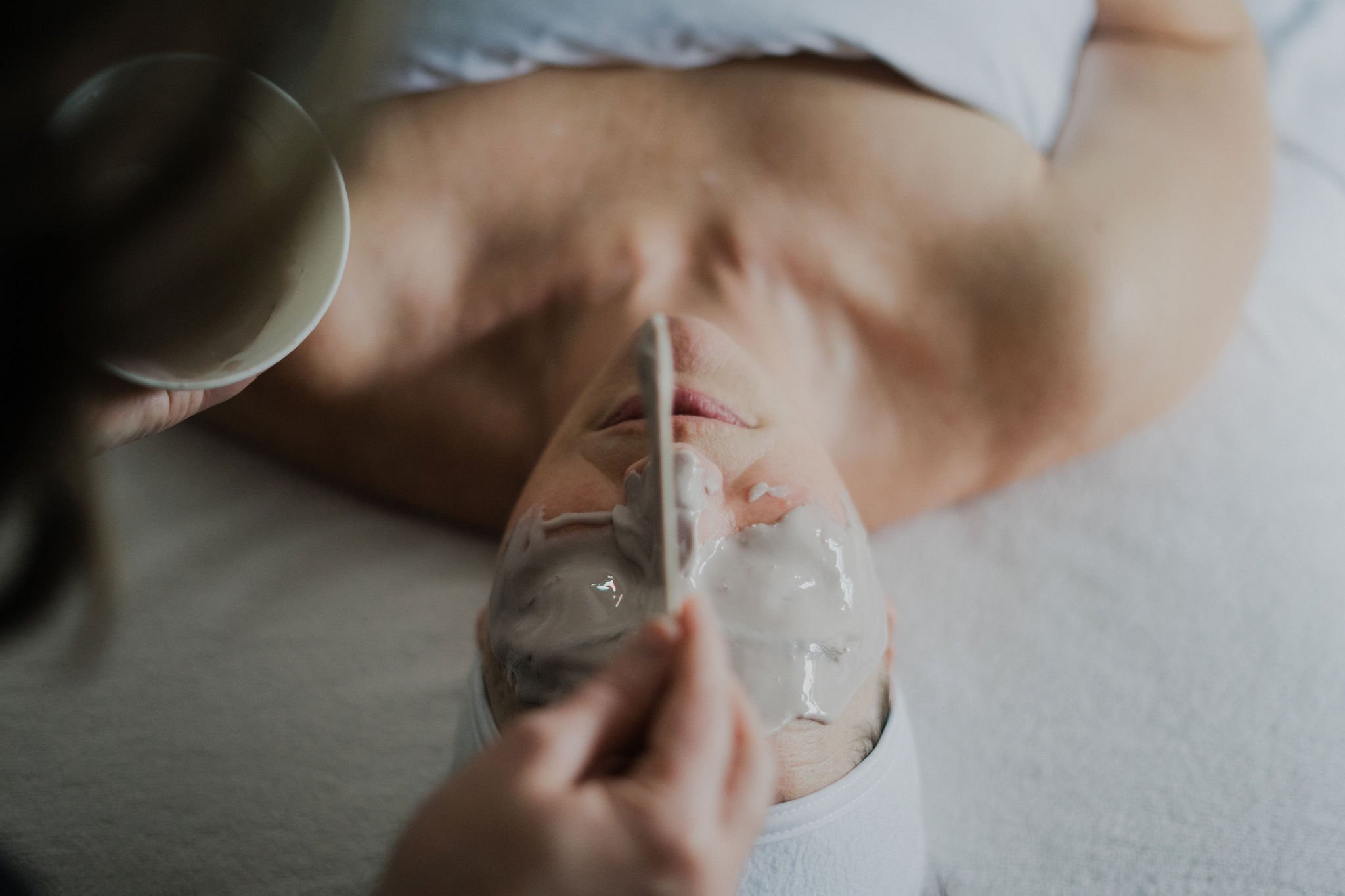 Woman receiving a facial treatment with jade rollers on her face, lying down with eyes closed.