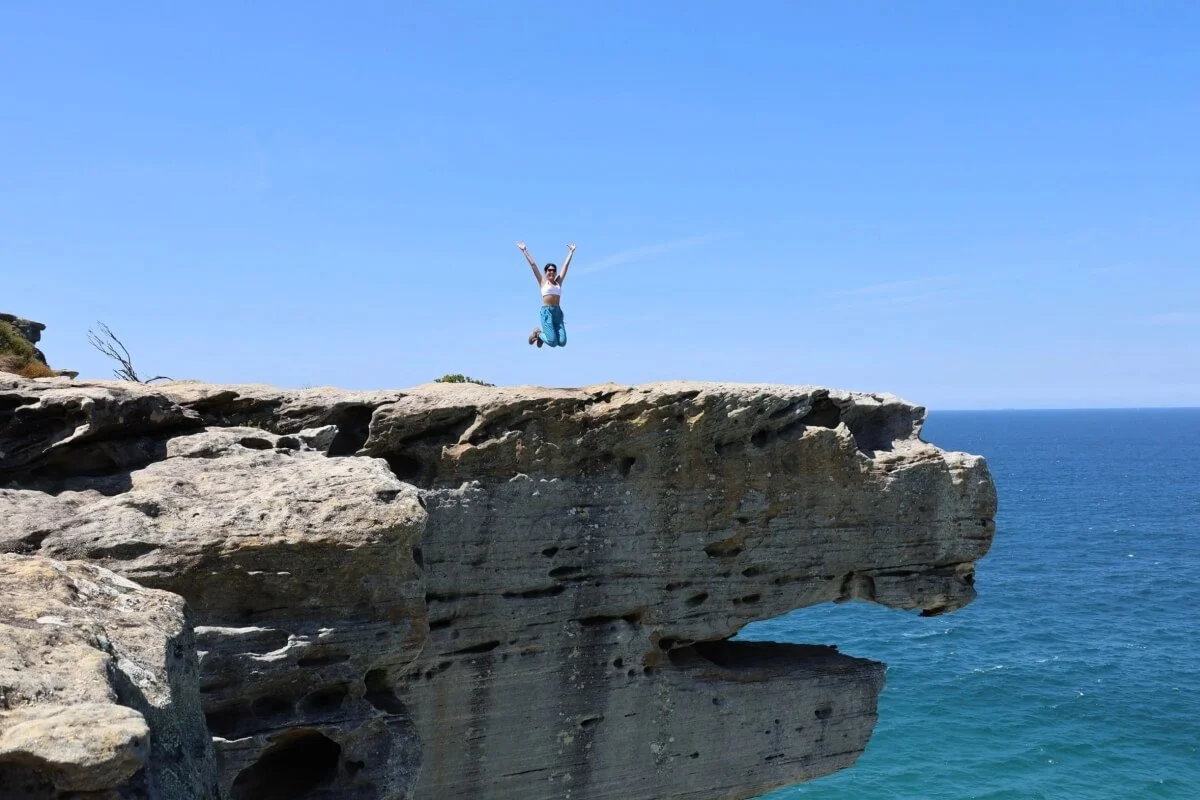 Guest jumping on top of Eagle Rock sandstone overhang above the Pacific Ocean, Royal National Park