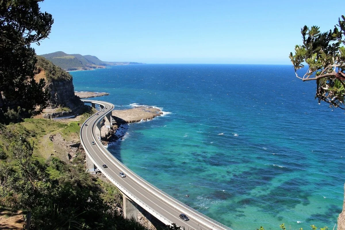 Aerial view of Sea Cliff Bridge curving along the NSW South Coast on Lawrence Hargrave Drive, with turquoise water and coastal cliffs