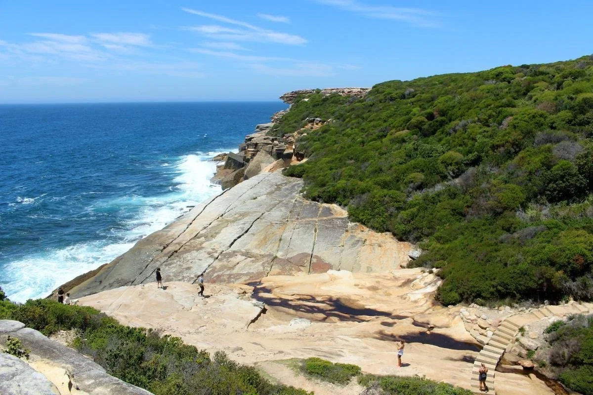 Visitors on the sandstone rock platform approaching Wedding Cake Rock, Royal National Park coastal walk