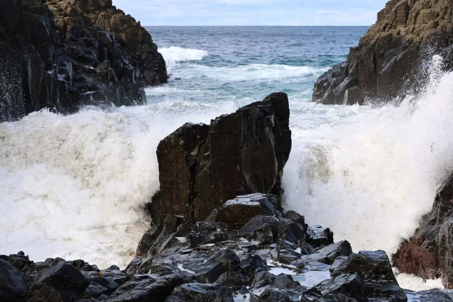 Ocean waves crashing through a channel in the basalt rock platform at Bombo Headland Quarry, Kiama