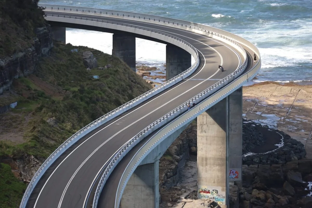 Close aerial view of Sea Cliff Bridge showing the tight double curve above rock platforms and ocean, NSW