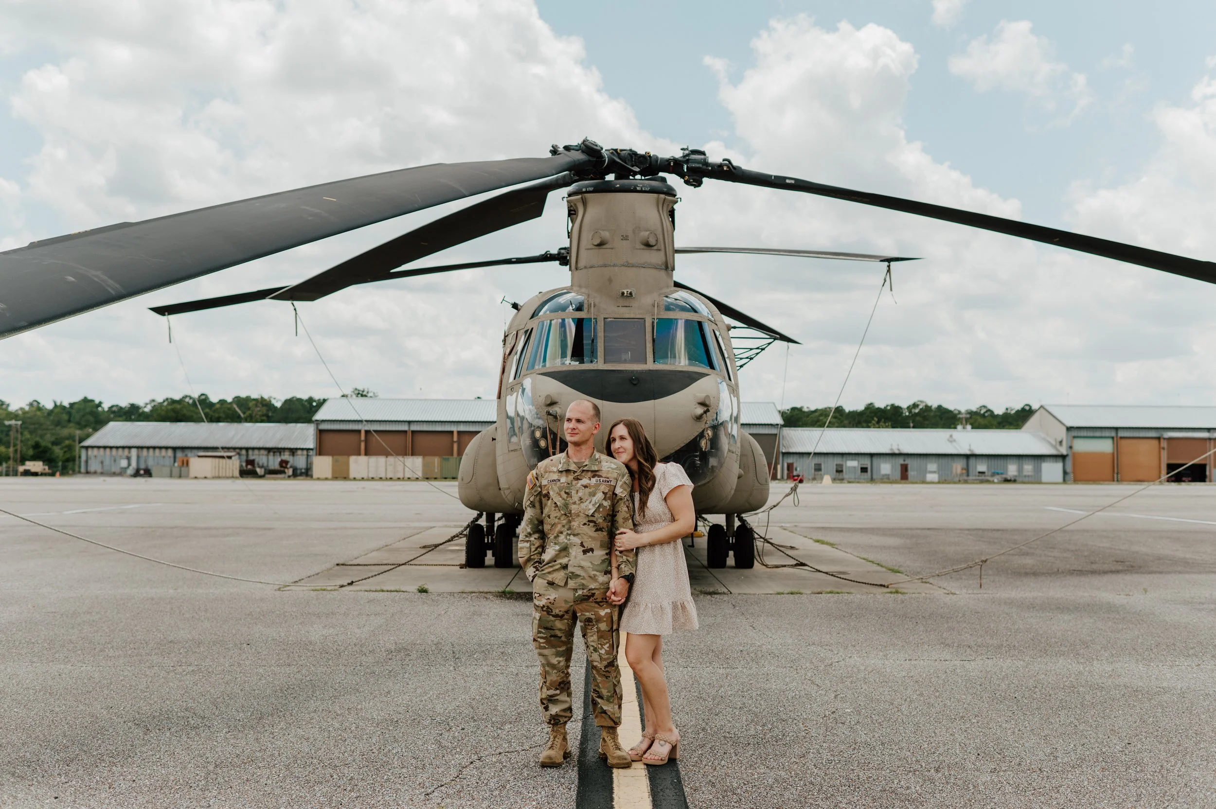 A soldier in uniform and a woman in a dress standing together in front of a military helicopter on an airfield.