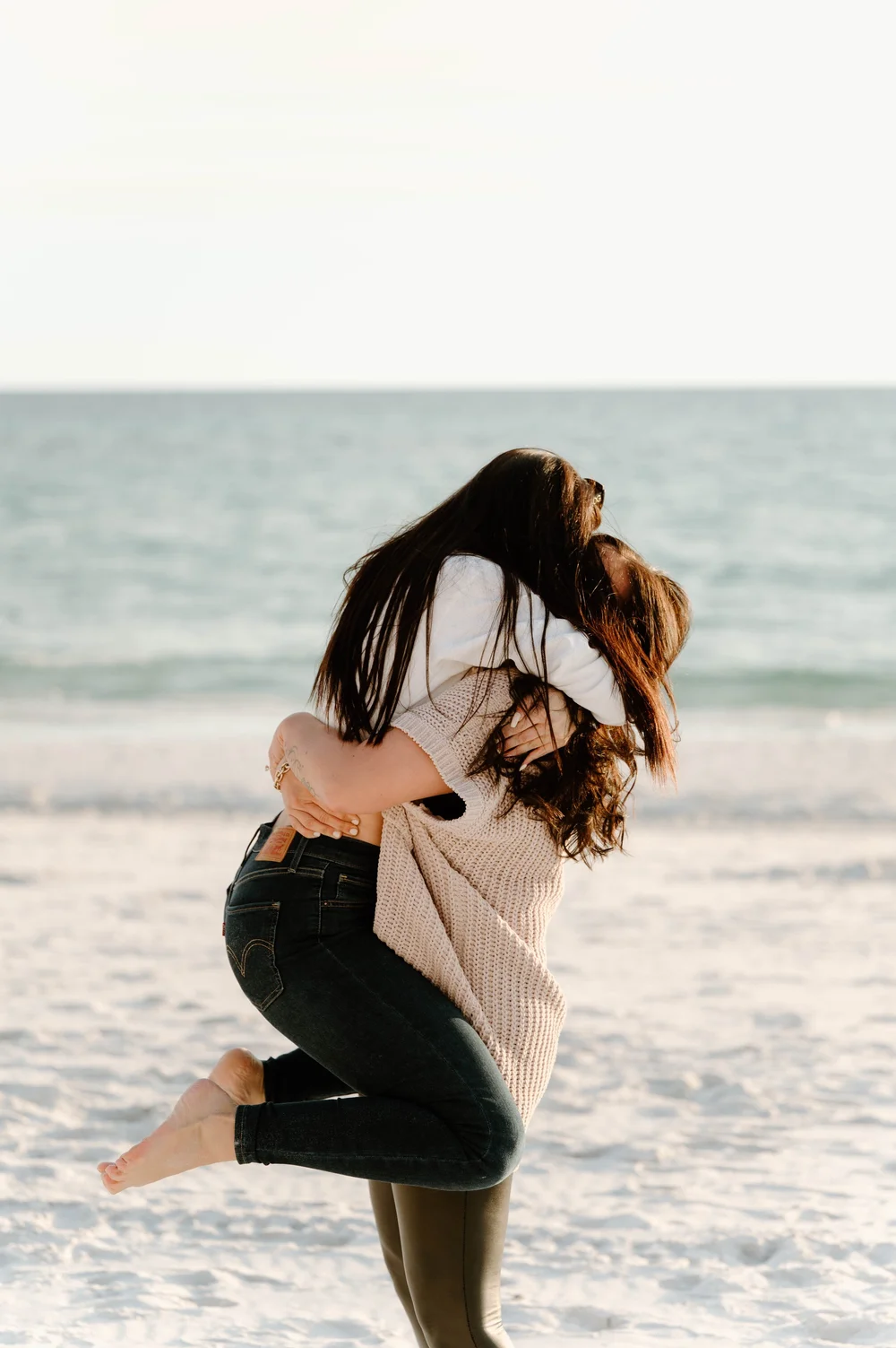  Two extrememly happy women hug on a beach at sunset  