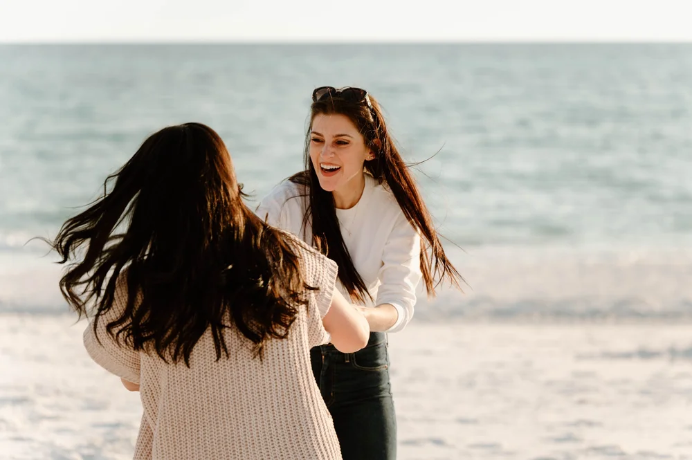  Two woman spin on a beach at sunset in pants and long sleeves 