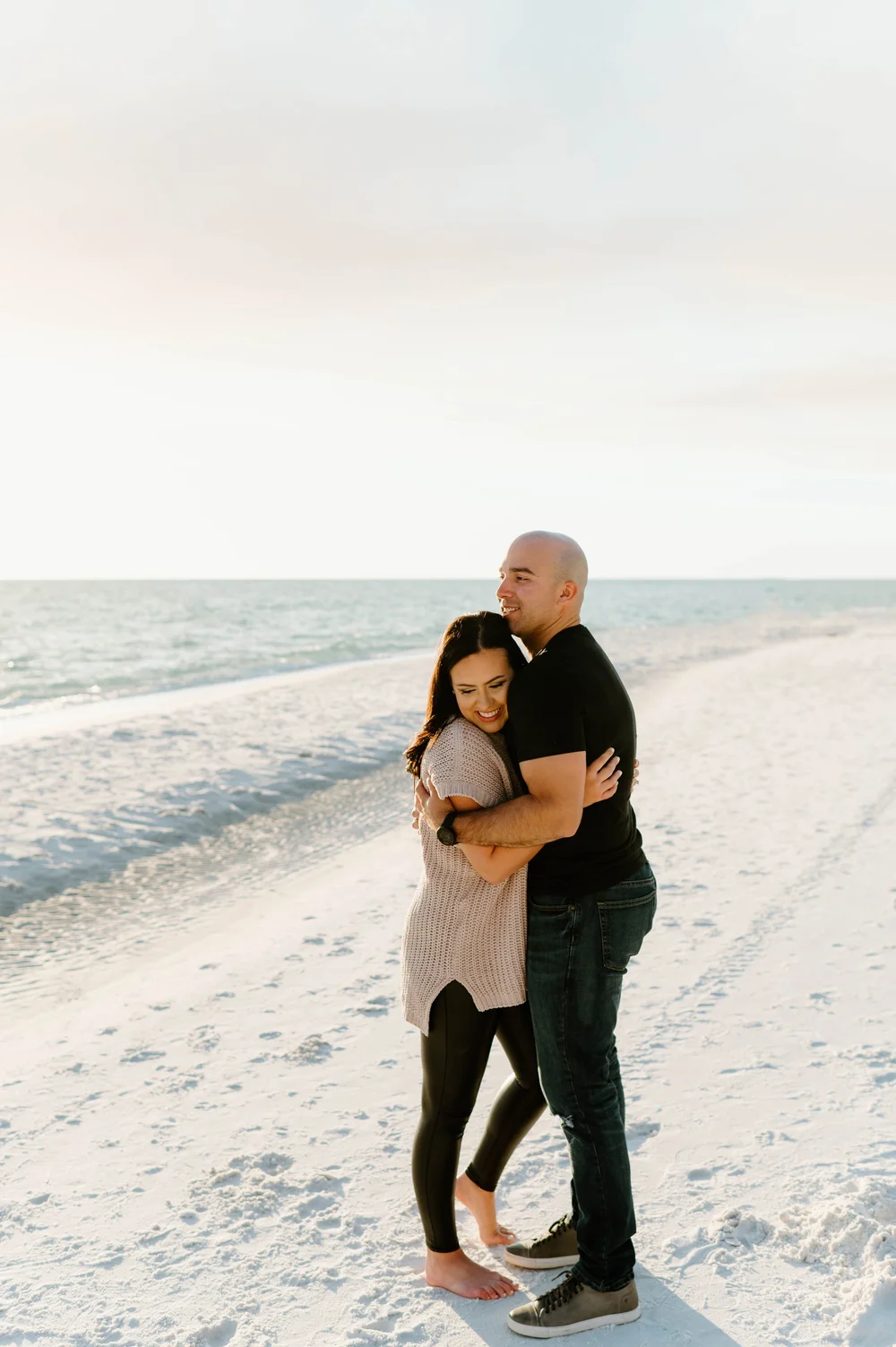  A happy couple hug on a beach while wearing tan and black after a magical 30A Proposal 