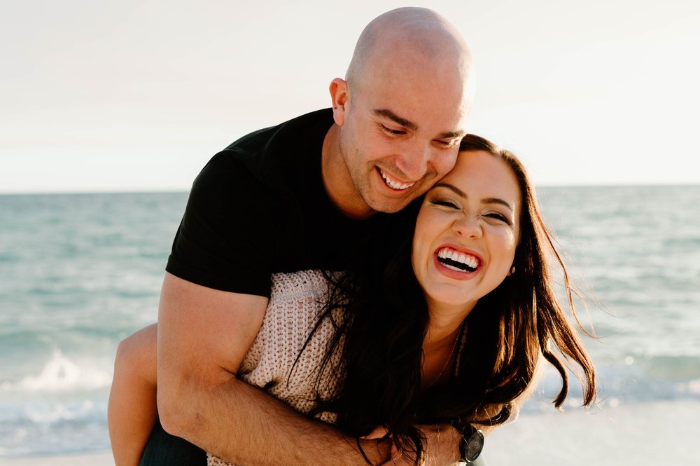 A happy couple laughs while playing on a beach at sunset  