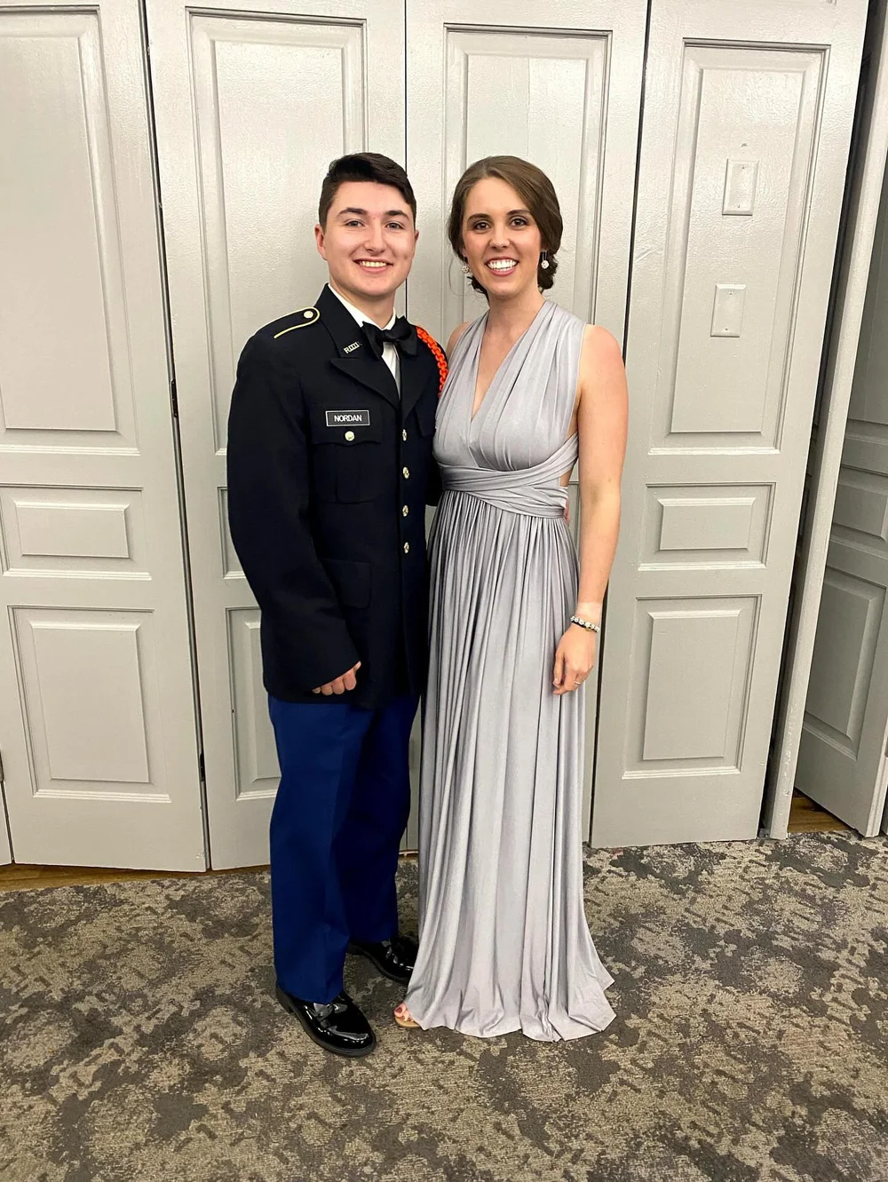  A woman in a grey gown stands with her officer partner smiling 