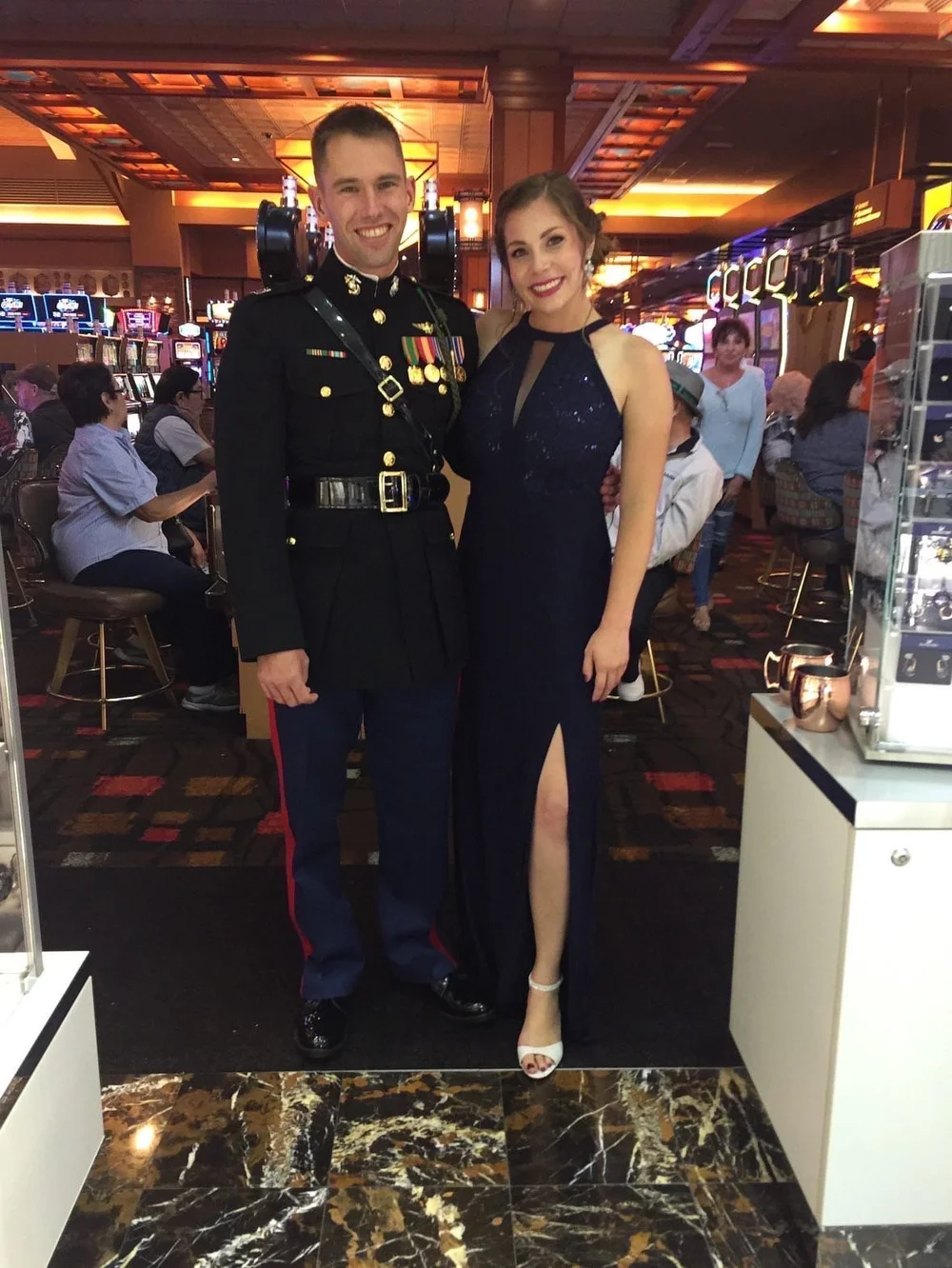  An officer and his wife wearing a black dress stand in a casino smiling  