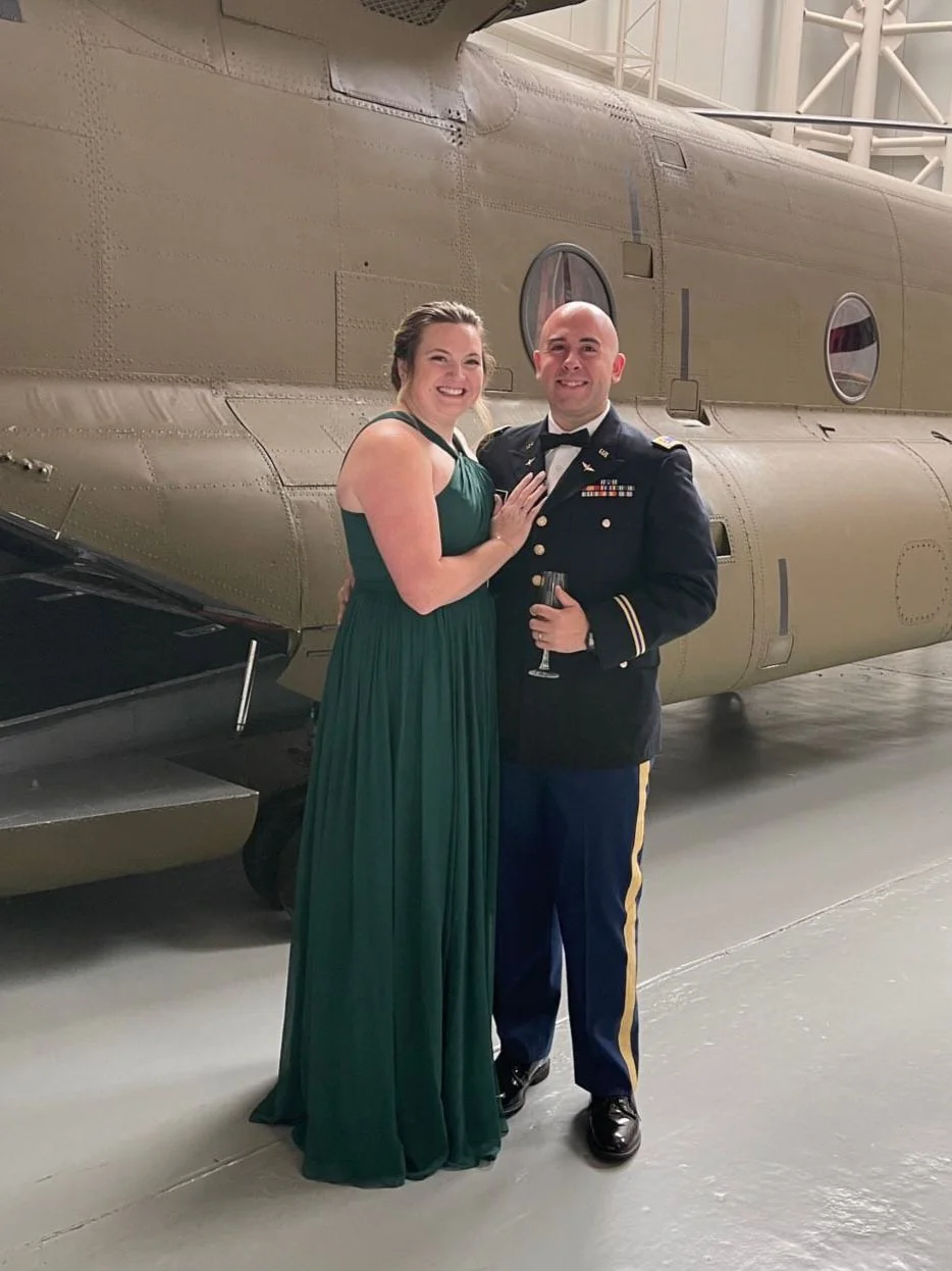  An officer and his wife in a green dress stand by a helicopter while celebrating his Military Graduation 