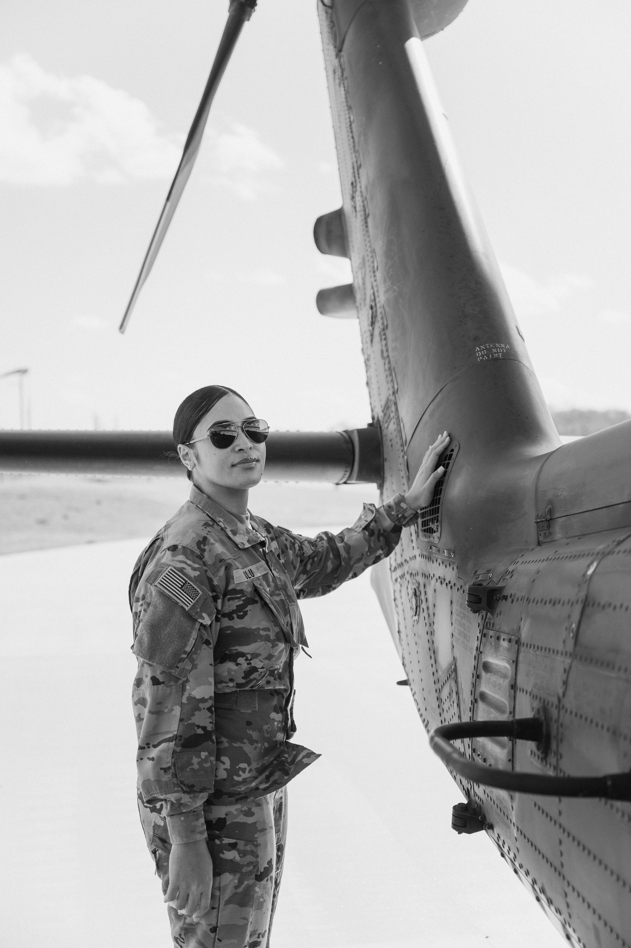 A female soldier in camouflage uniform and sunglasses touching the side of a military helicopter