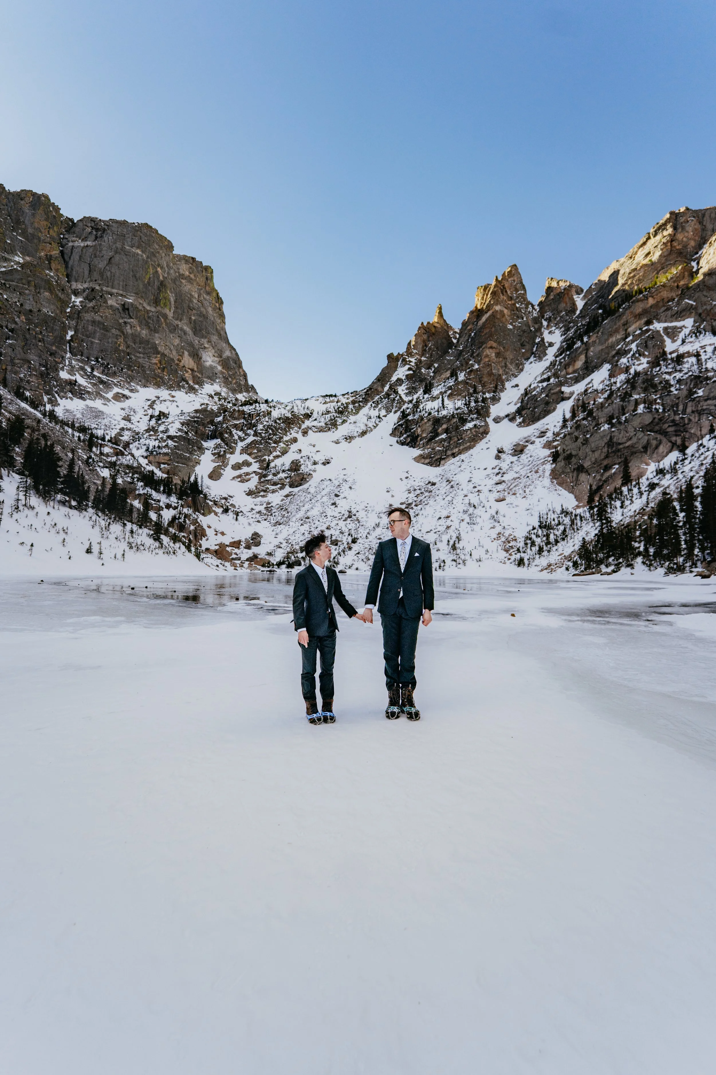 Two grooms hand and hand standing on the ice of Emerald Lake in RMNP in Colorado