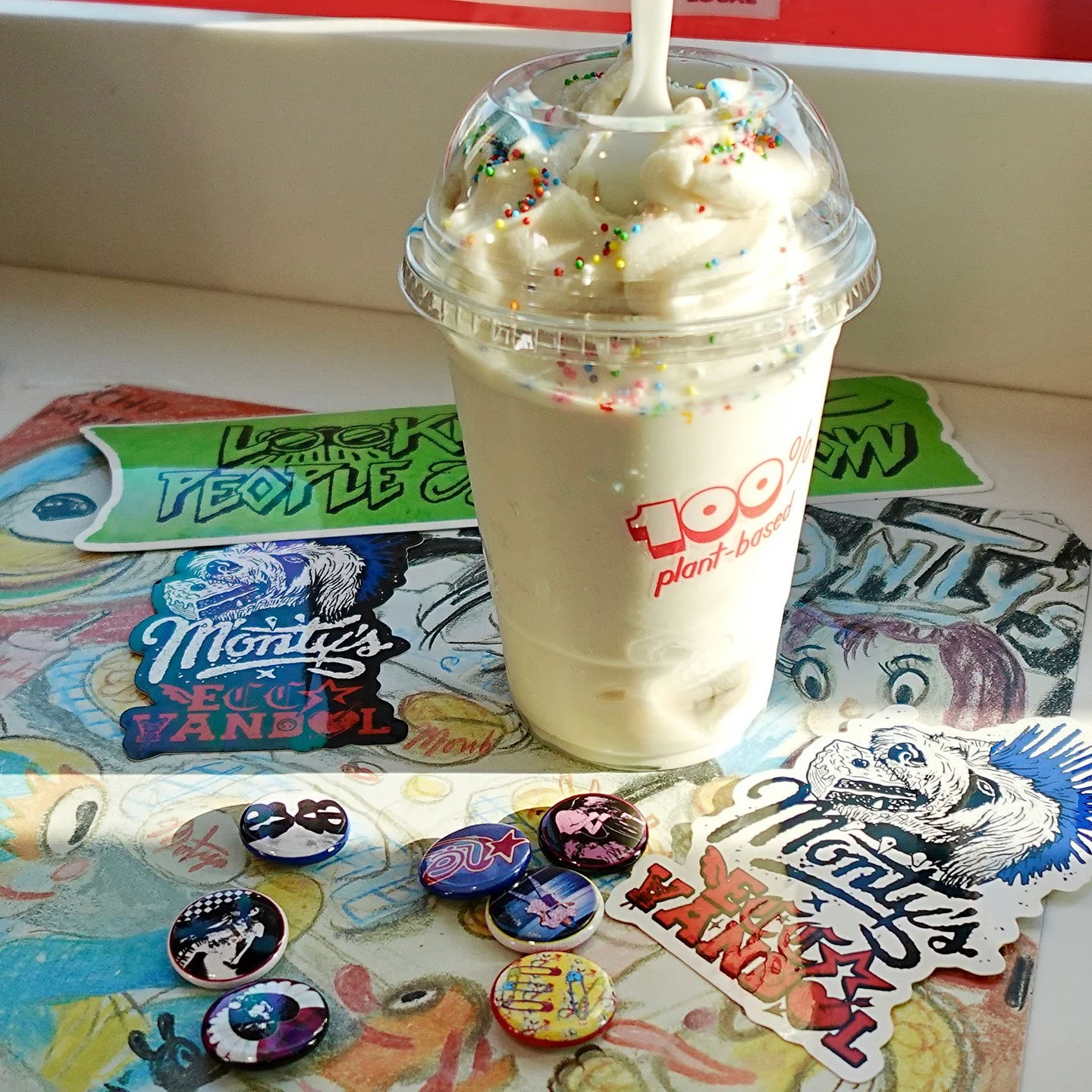 A thick, creamy Monty's plant-based shake topped with colorful sprinkles and a spoon, sitting on a colorful punk-rock sticker counter in Los Angeles.