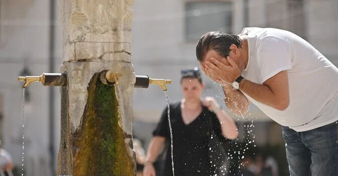 A man cooling his face with water from a public fountain during extreme summer heat in Europe.