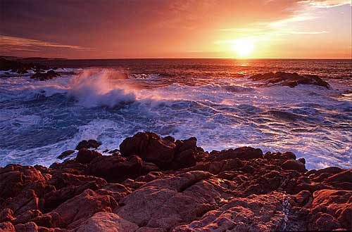 The sun's light glows red at sunset because the shorter blue wavelengths have been lost due to scattering. *Note however that the scattered blue light is reflecting back from the eastern sky and acting as a fill on the foreground waves.