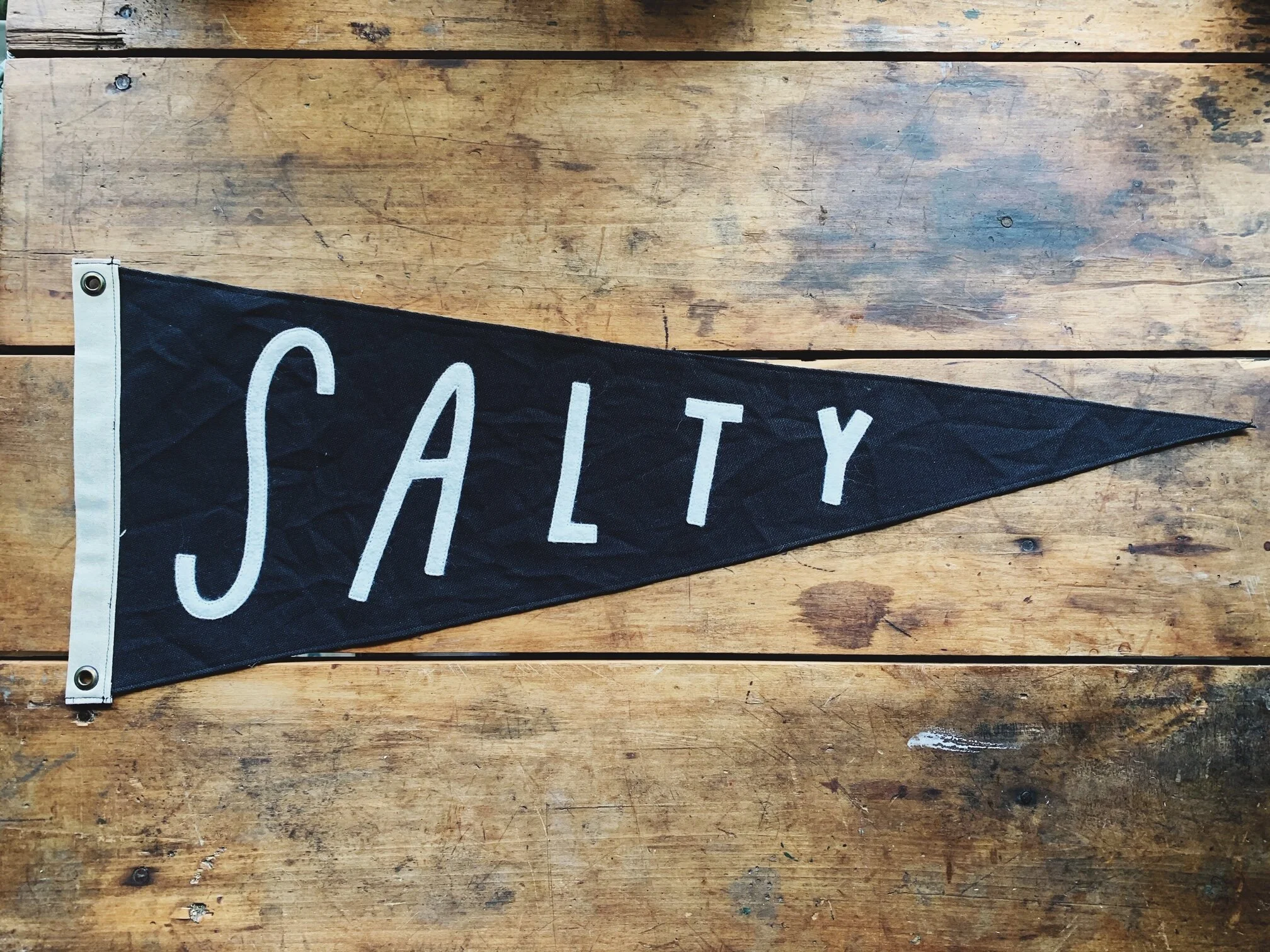 A black triangular flag with the word 'SALTY' in white letters, laid on a wooden surface.