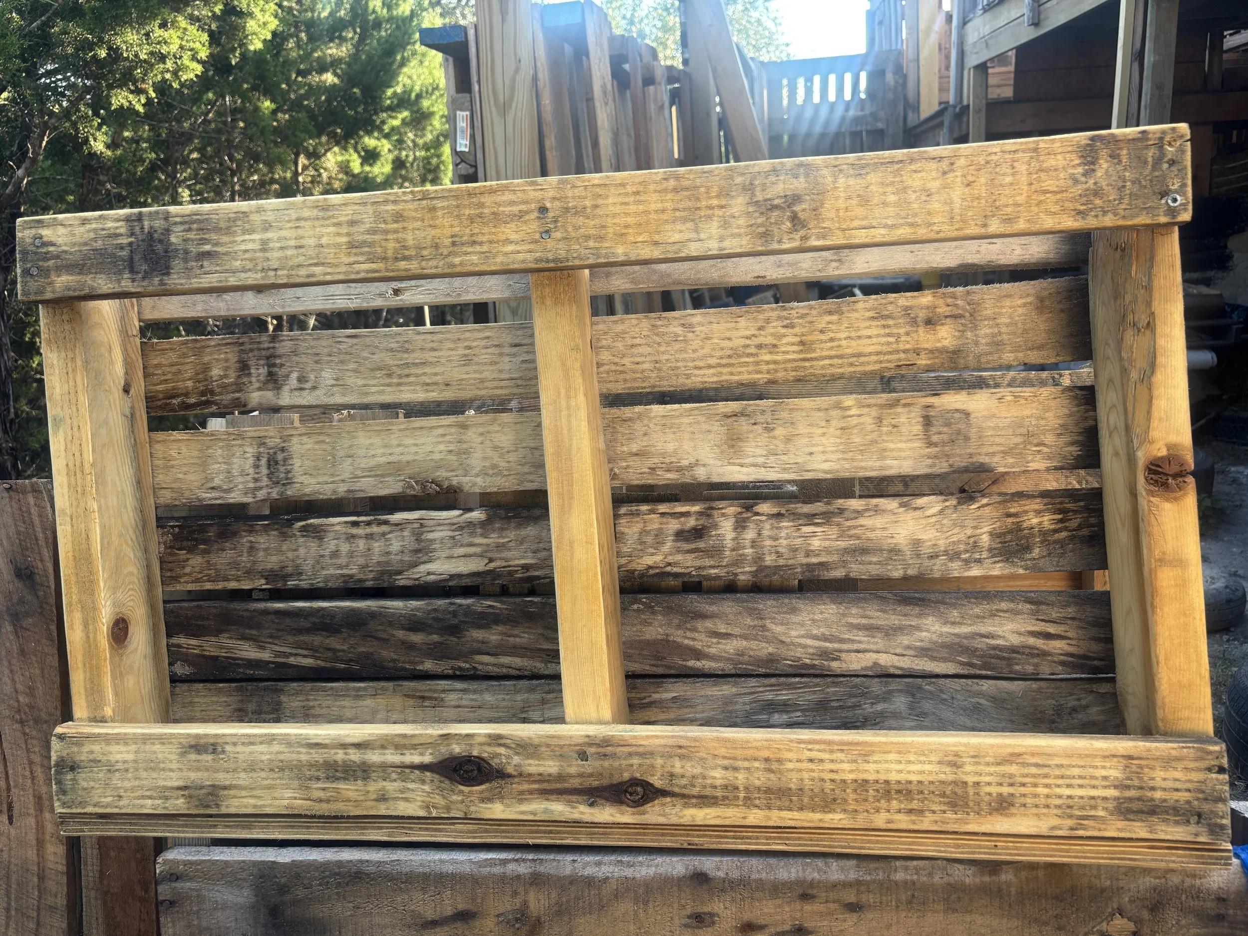 Wooden garden fence with horizontal planks and vertical posts, outdoors with trees and sunlight.