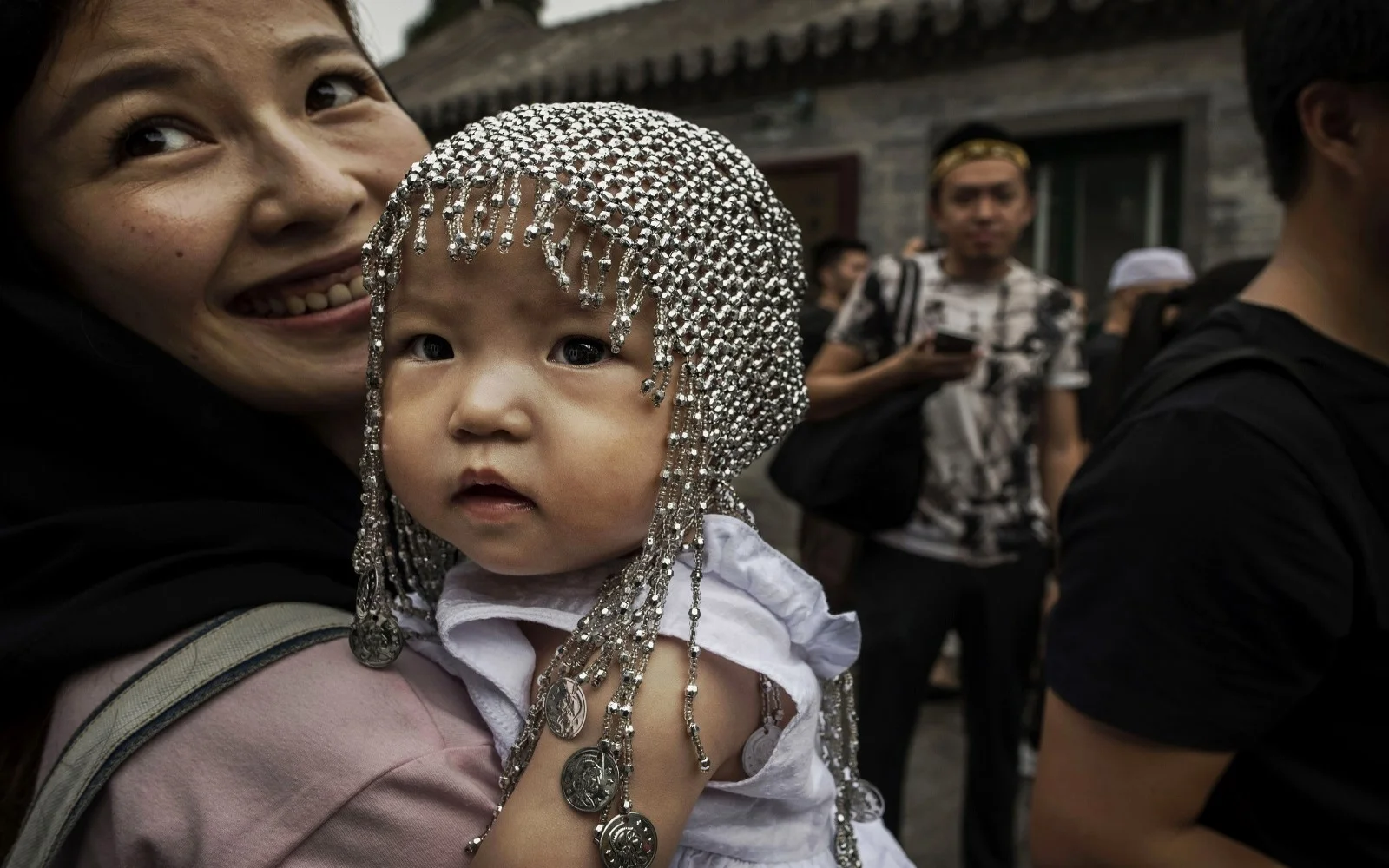 A Chinese Hui Muslim girl wears a fancy headdress as she is held by her mother after Eid al-Fitr prayers marking the end of the holy fasting month of Ramadan at the historic Niujie Mosque on June 16, 2018 in Beijing, China. (Photo by Kevin Frayer/Getty Images)