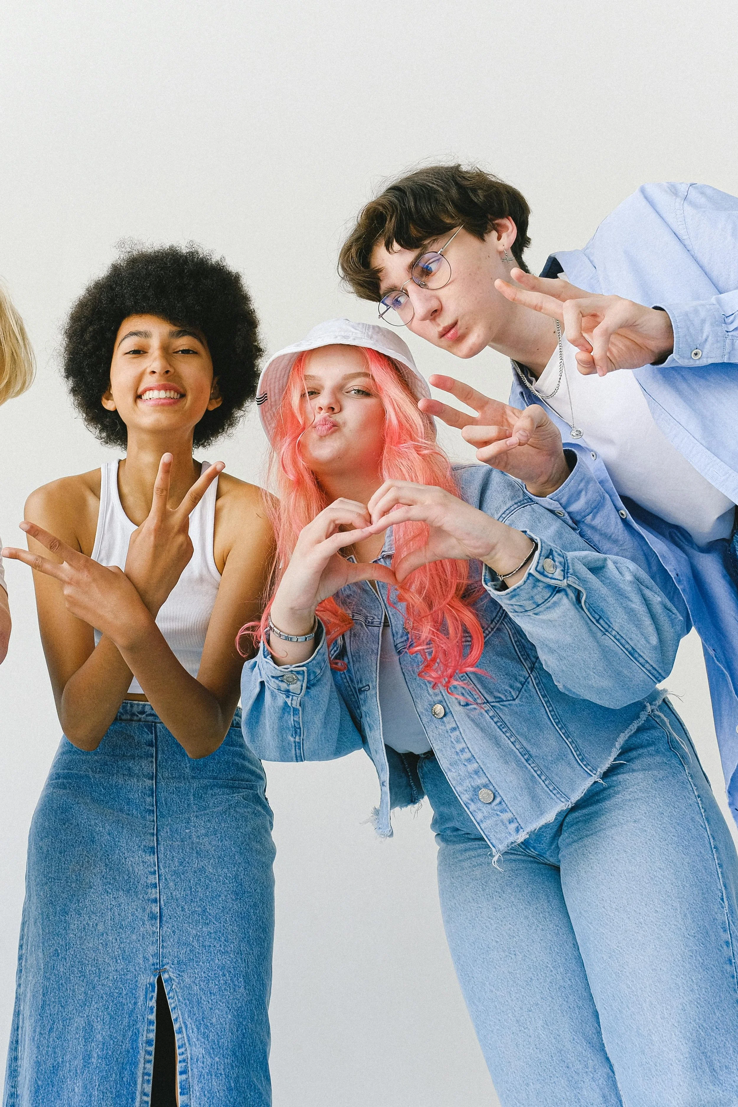 Group of four diverse young people making peace signs, smiling, and posing in front of a plain white background.