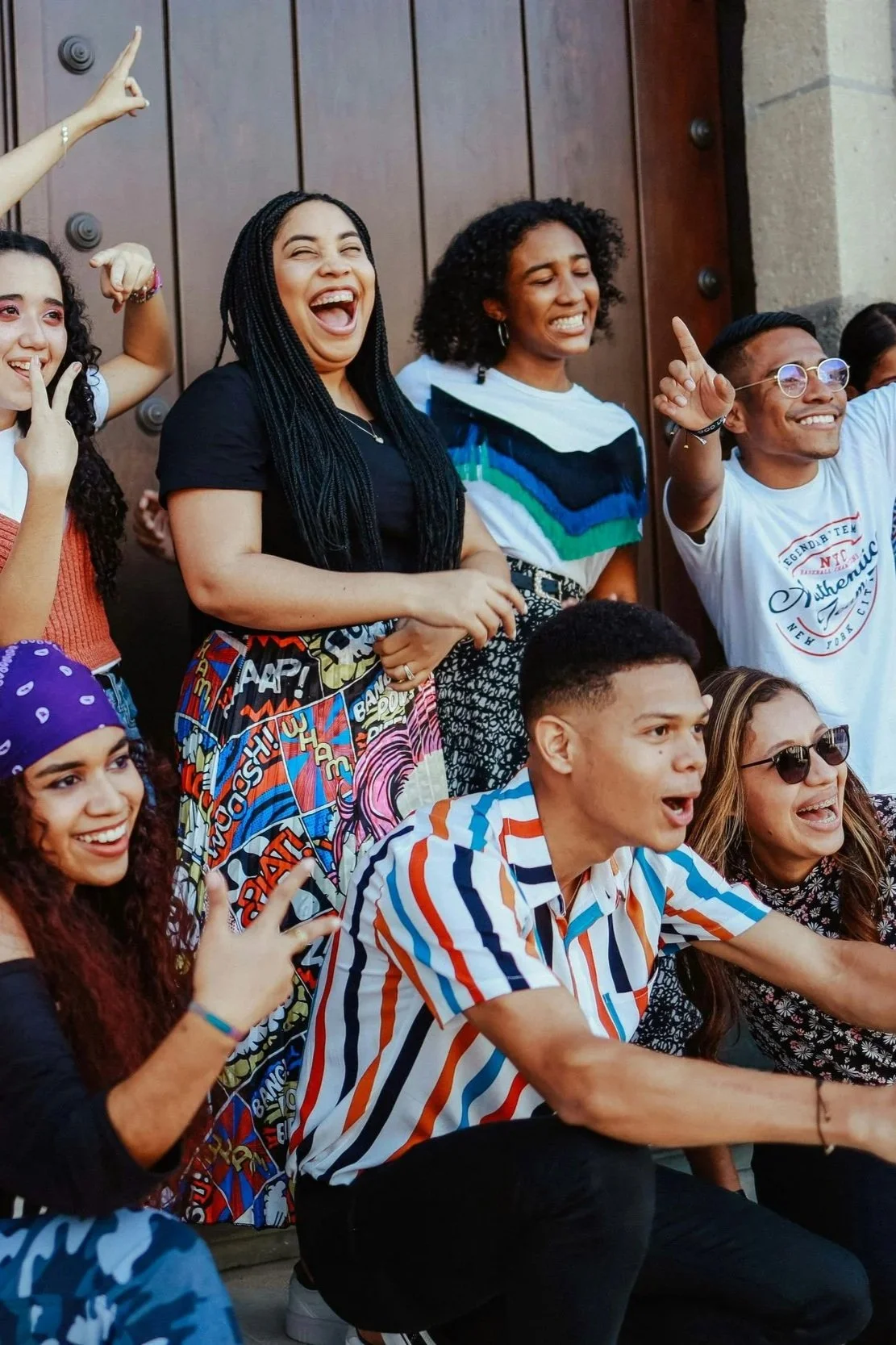 Group of diverse young people enjoying and laughing outdoors with a wooden door in the background.