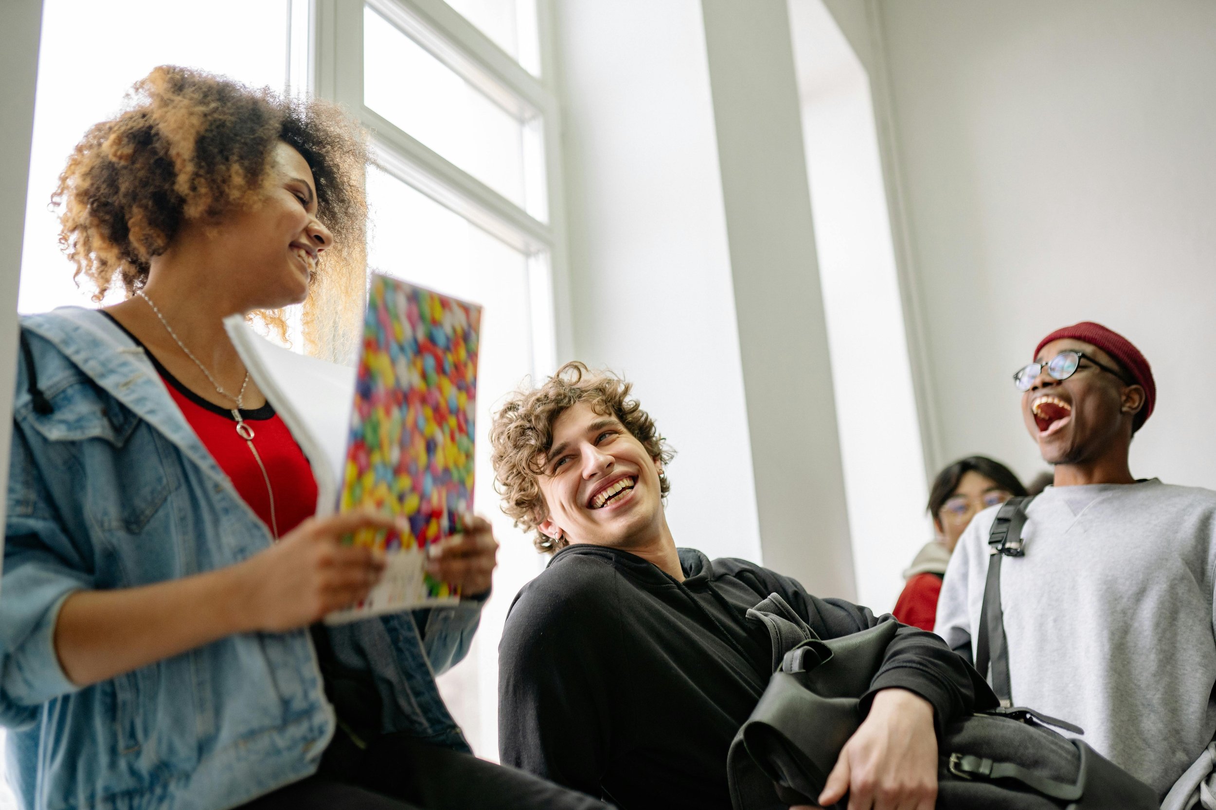 Group of young people enjoying a social moment indoors, smiling and laughing with one holding a colorful gift bag.