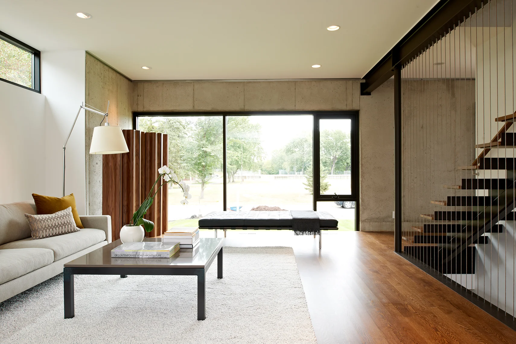 Modern living room with wood floor, concrete wall, and custom open stair