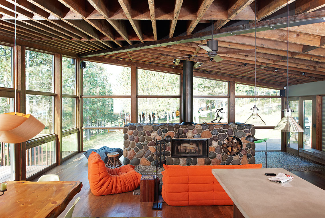 Center pebble fireplace with reclaimed timber ceiling in a cabin living room