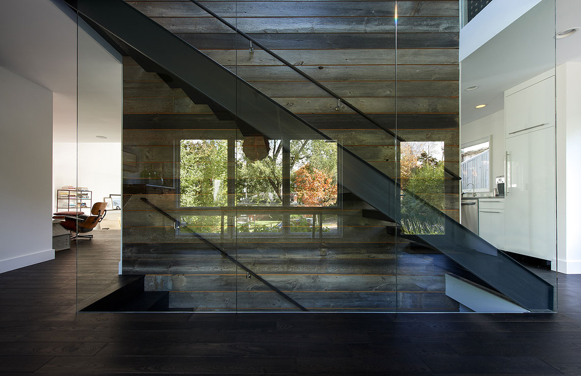 Modern staircase between glass and wood paneled walls