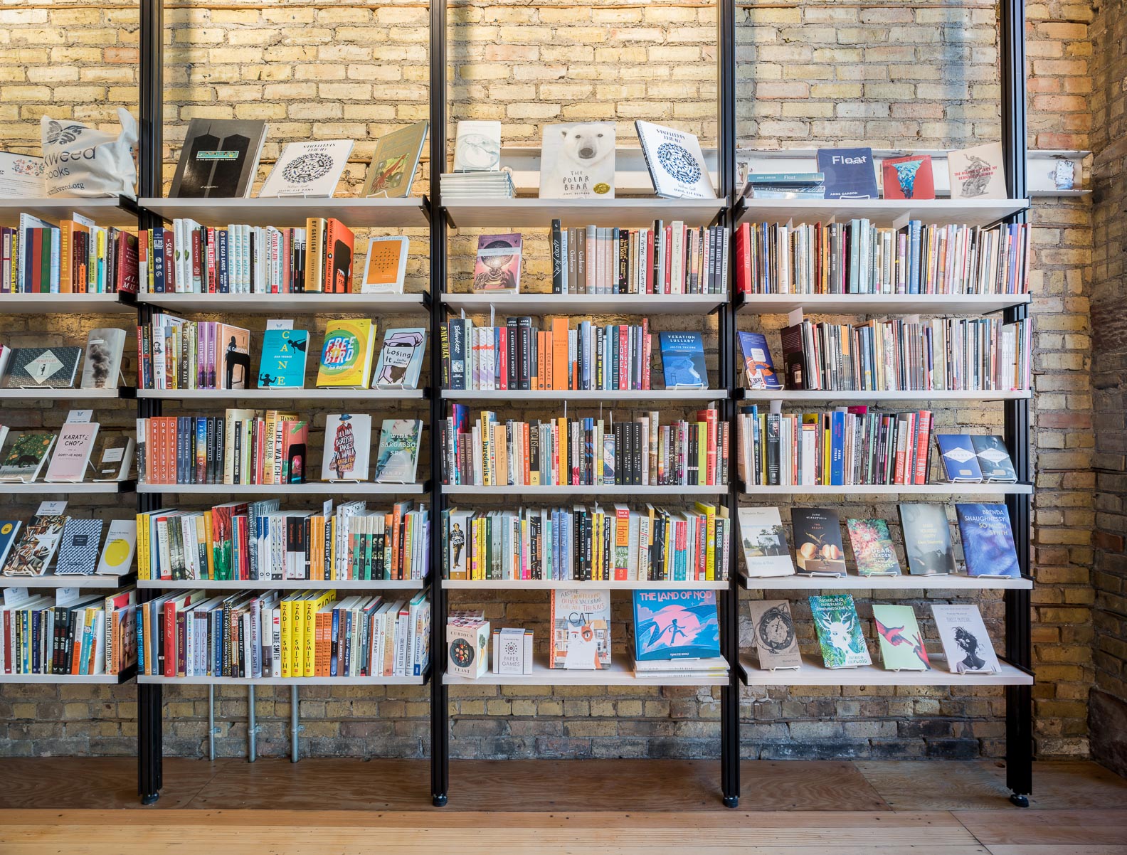 modern open steel and wood bookshelves against aged brick wall in milkweed bookstore minneapolis