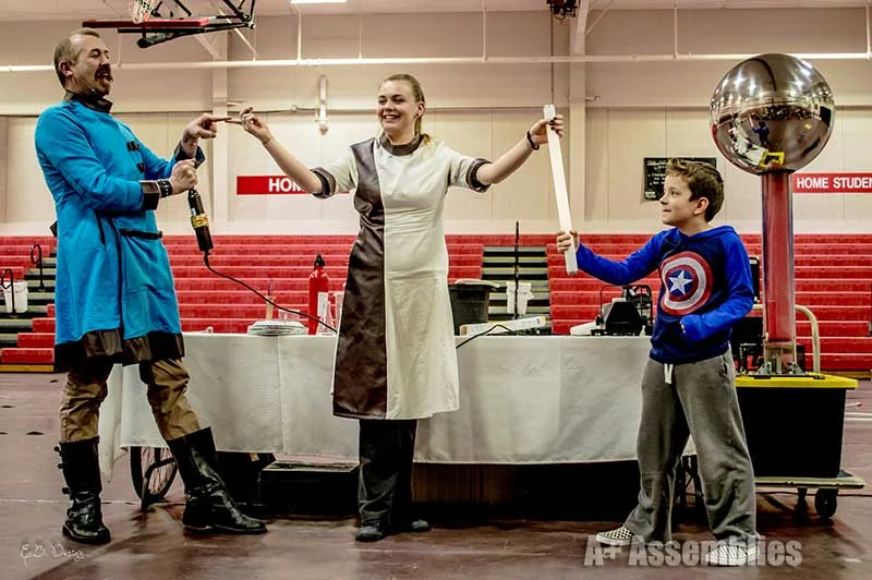 A Van de Graaff generator demonstration with a student volunteer at a school assembly in a gym