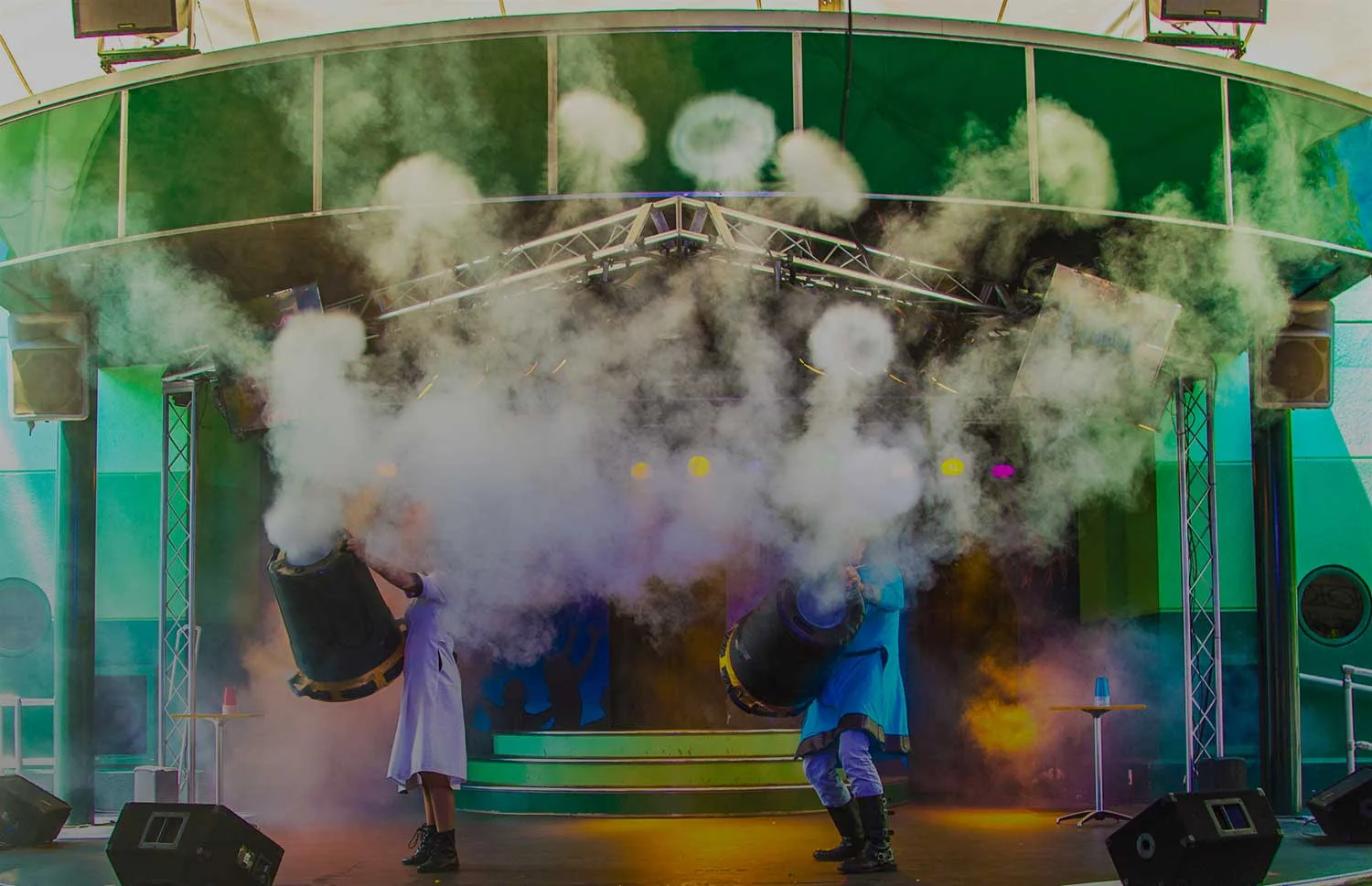 Two performers firing giant vortex cannons that send smoke rings over the audience at a school science assembly