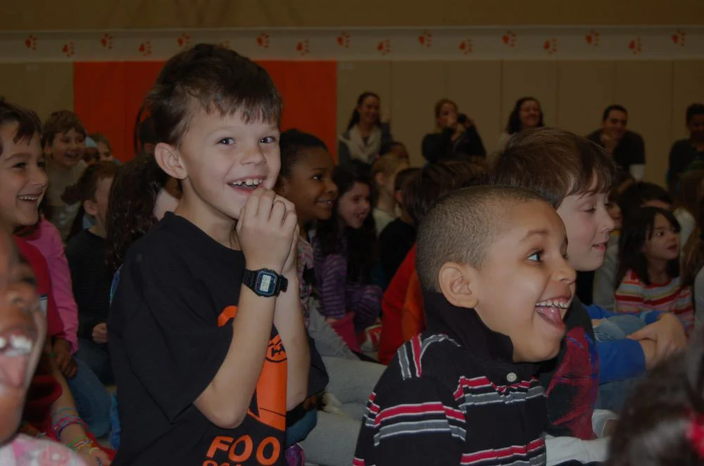 Grinning elementary students in the audience at a school assembly
